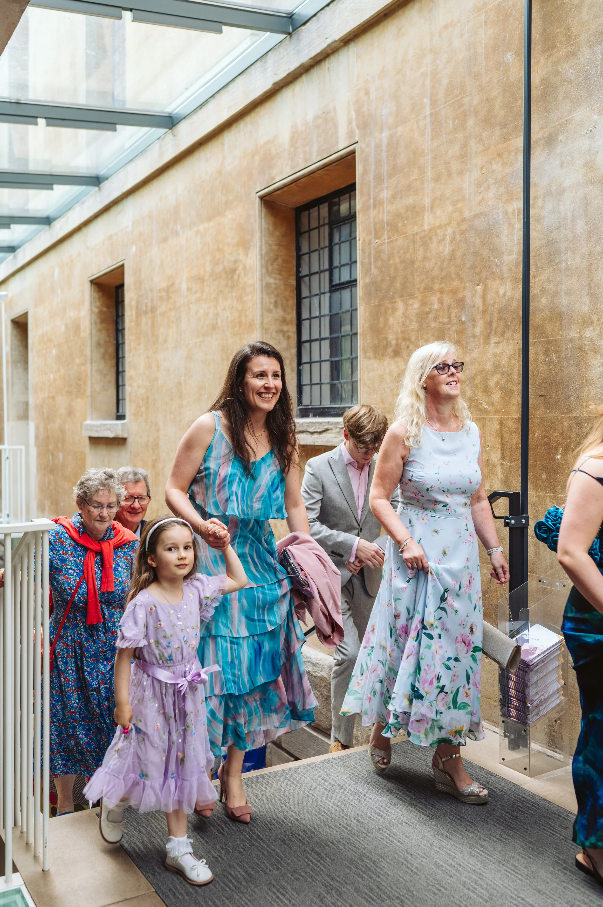 A group of people, including women and children, walking through a glass-roofed corridor with stone walls.