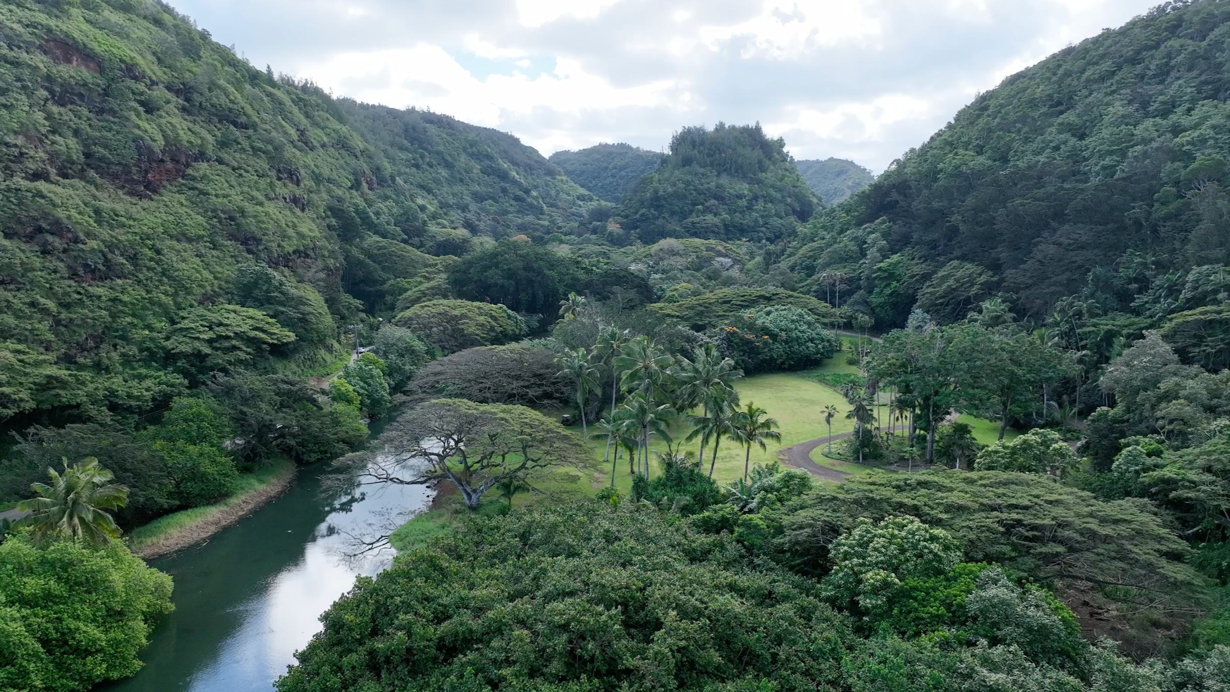 Scenic landscape with a large stream surrounded by tall, lush green mountains under an overcast sky.