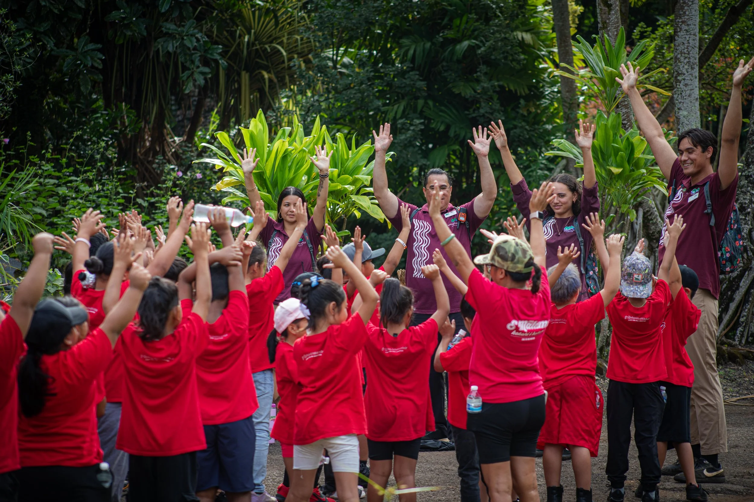A large group of children standing in front of Waimea Valley Educators with hands up in the air 