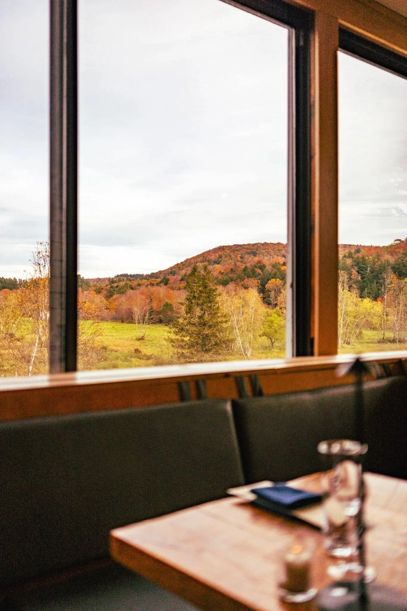 Open window showing a landscape of trees with colorful fall foliage and a hill in the distance, as seen from a conference room or office with black chairs and a table with a glass of water, a smartphone, and a notepad on it.