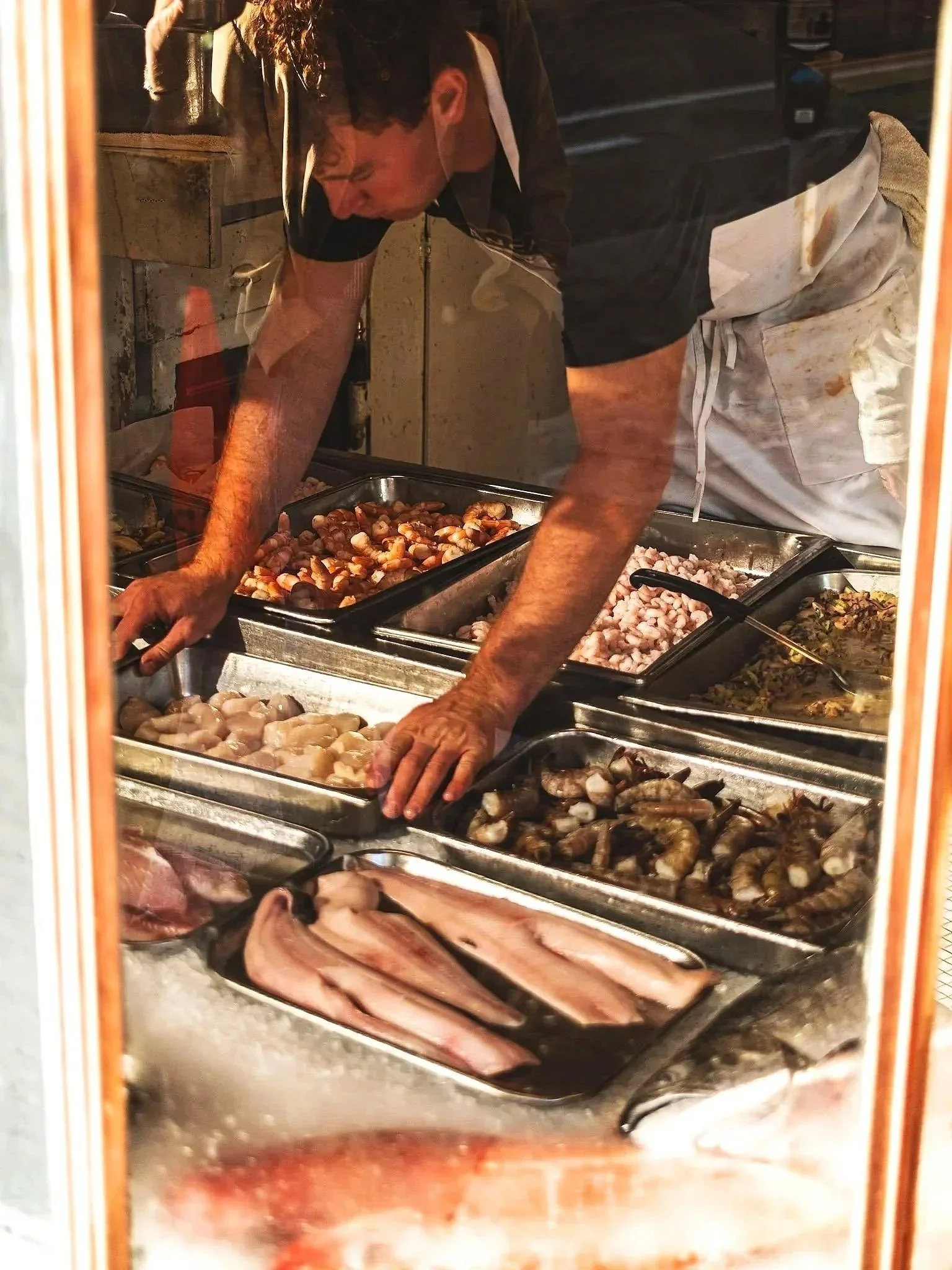 A person arranging seafood including shrimp, fish, and other shellfish at a seafood counter in a market.