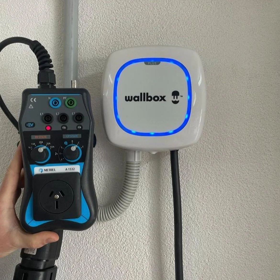 Electrical charger mounted on a wall, with a device connected to it for charging.