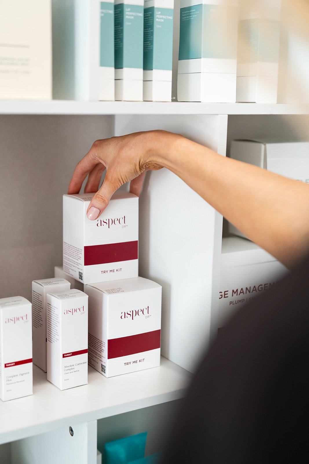 A person's hand reaching for a white box labeled 'aspect DR' on a shelf with other similar boxes.