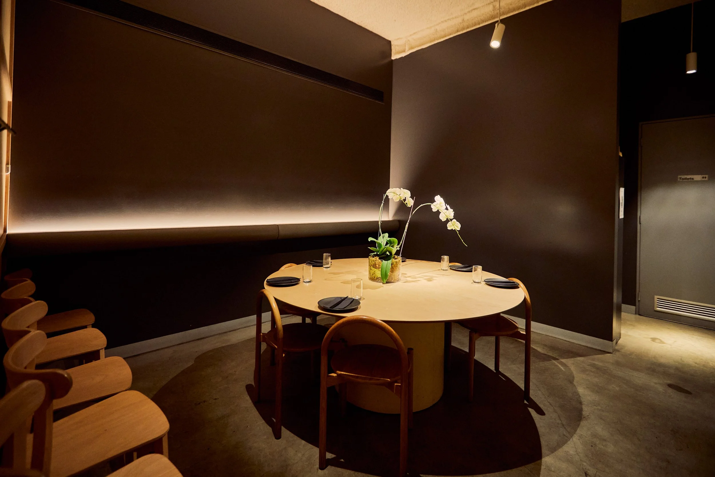Minimalist dining room with a round table and chairs set for dining, decorated with a potted plant.