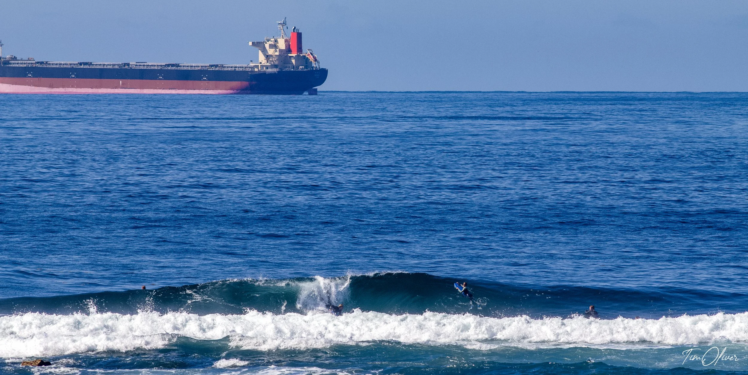 Bodyboarder surfing a reef with a massive ship in the background