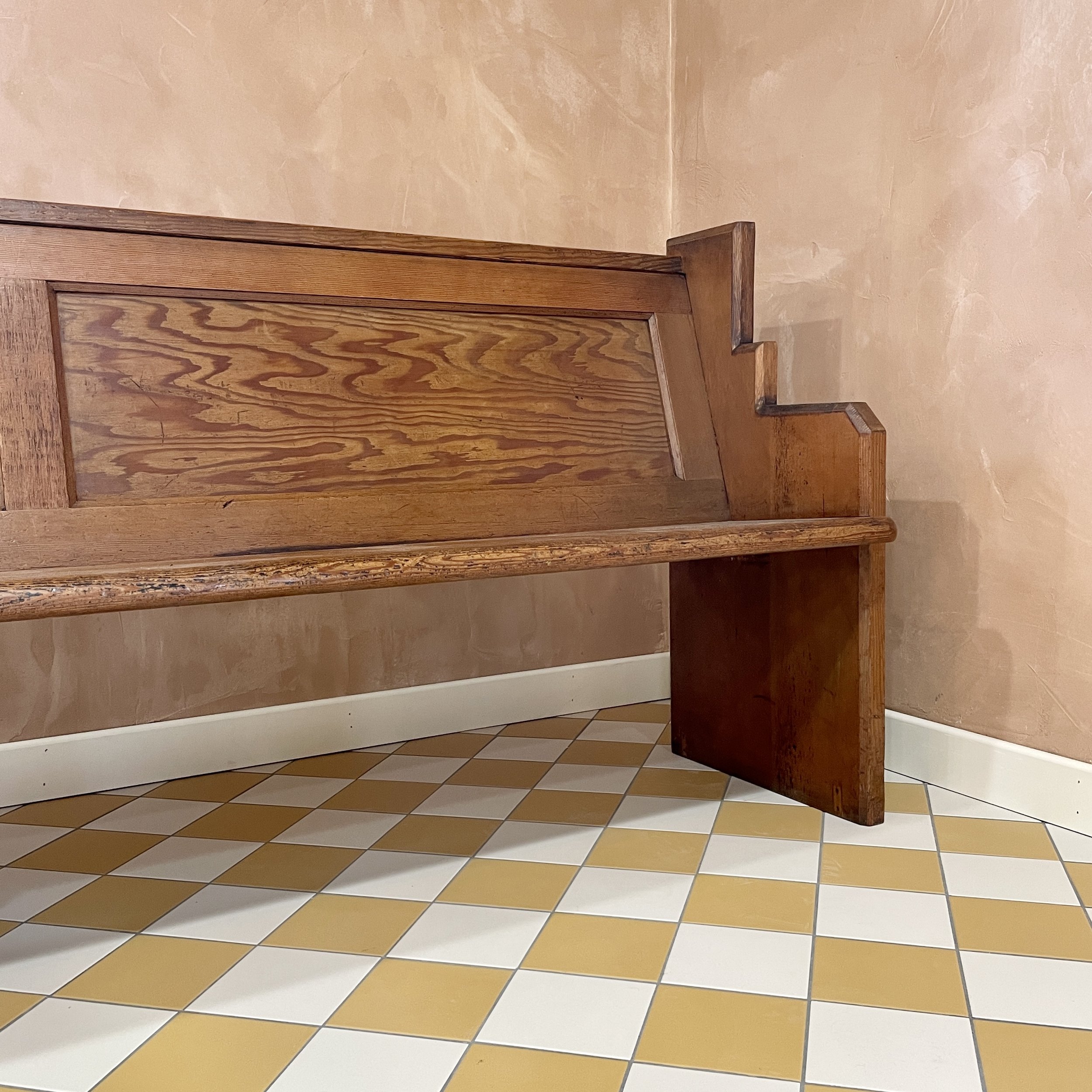 Wooden church pew against beige wall with yellow and white checkered tile floor.