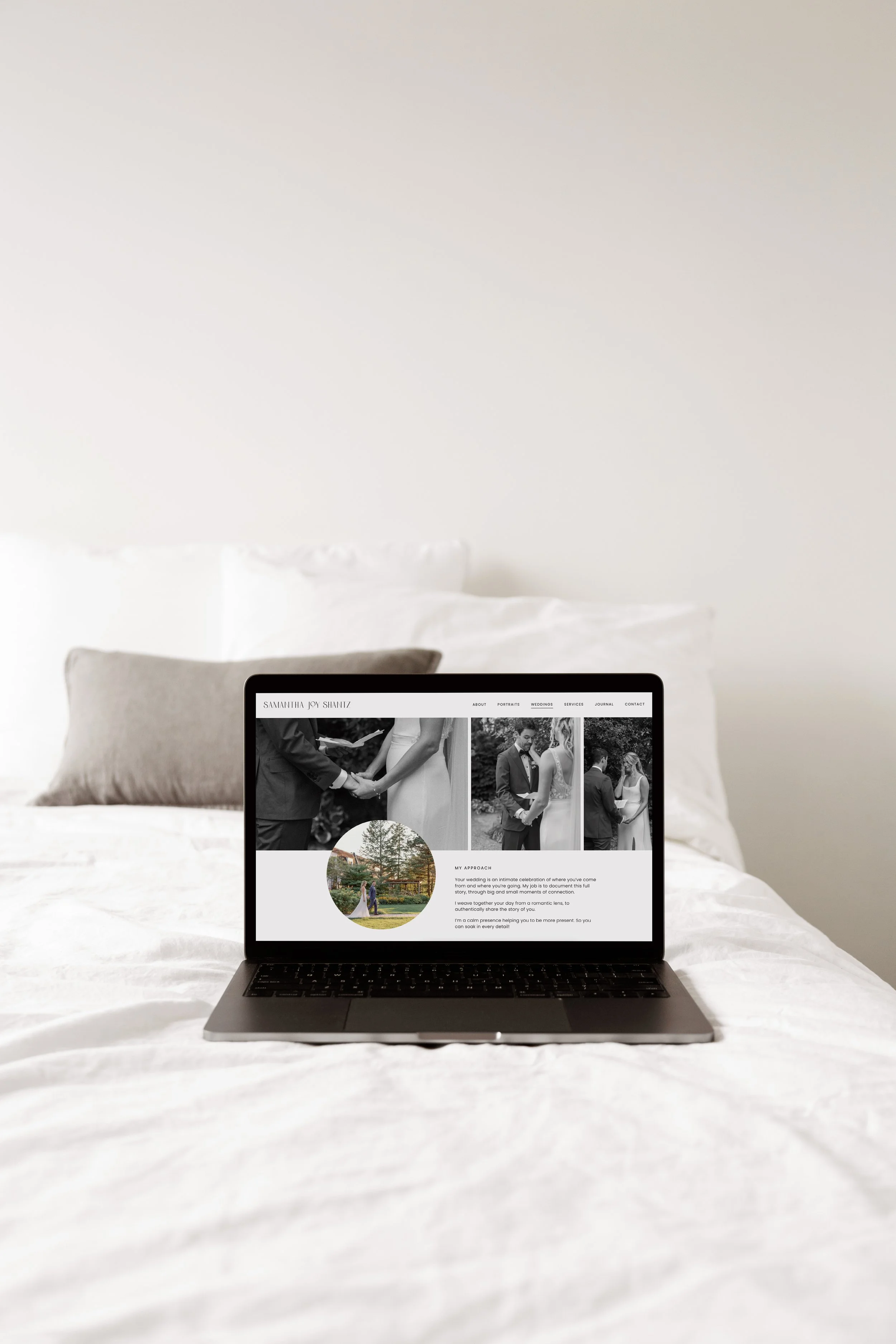 Laptop displaying a wedding photographer's website on a bed with white bedding.