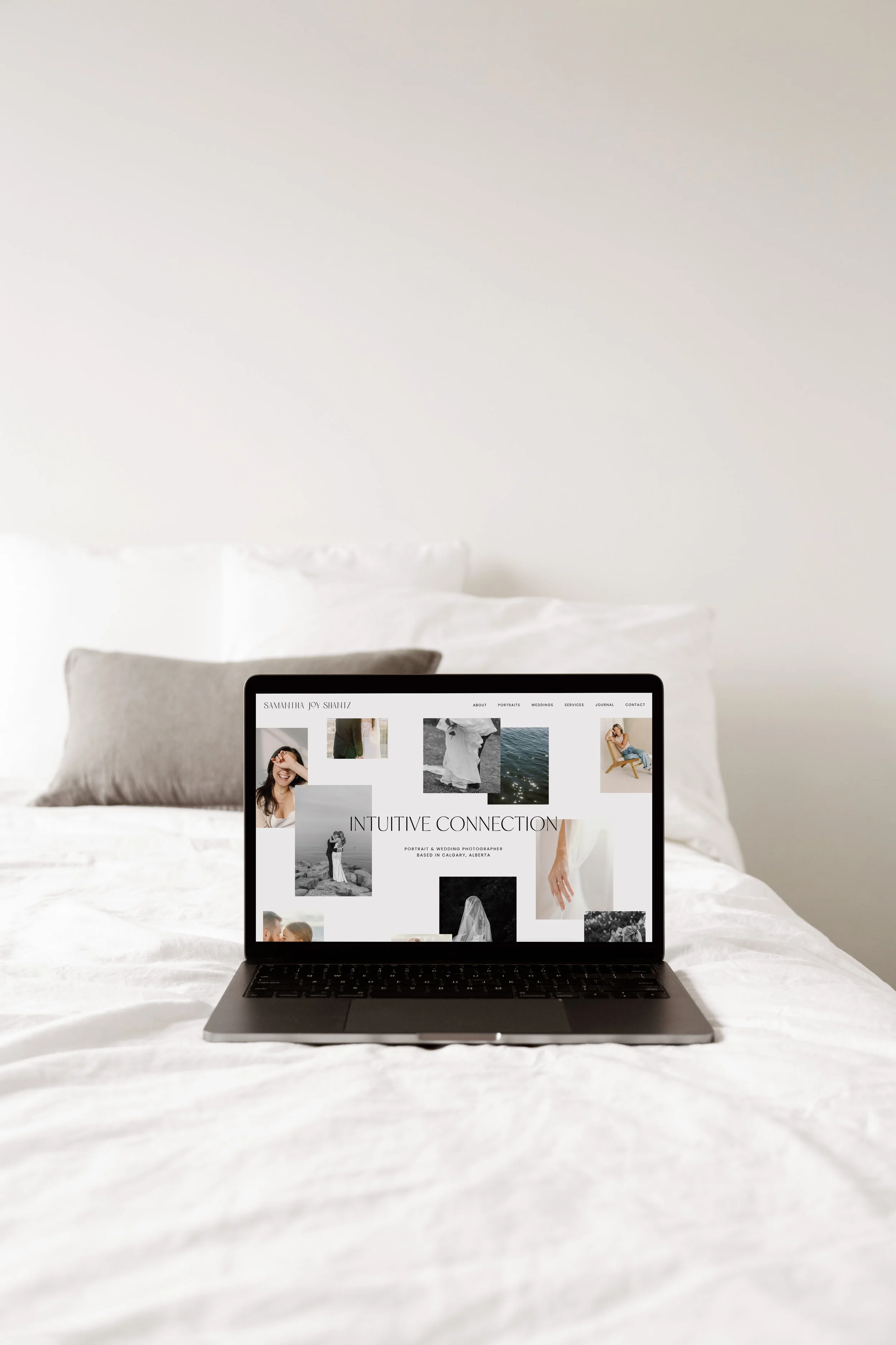 Laptop displaying a photography website on a bed with white bedding, featuring a collage of images and the text 'Intuitive Connection.'
