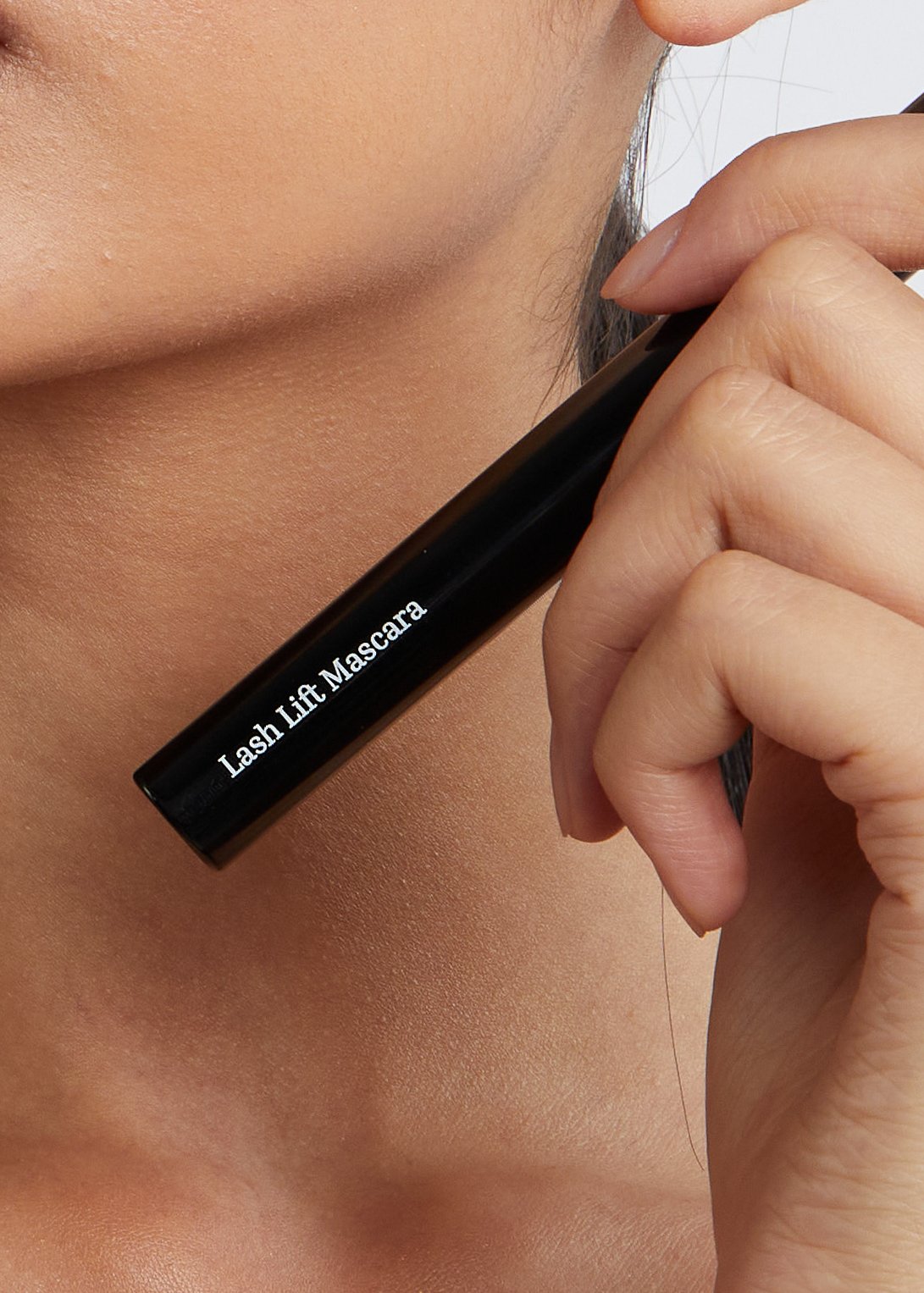 Person holding a black mascara tube labeled 'Lash Lift Mascara' near their cheek.