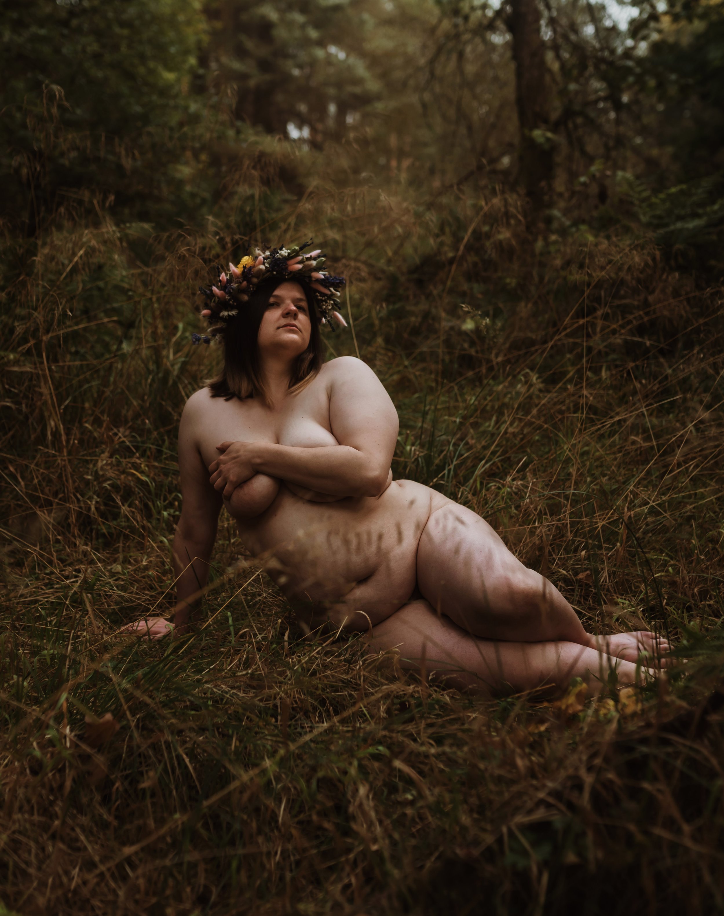 Outdoor boudoir photography Scotland — woman with flower crown seated in wild Scottish grassland