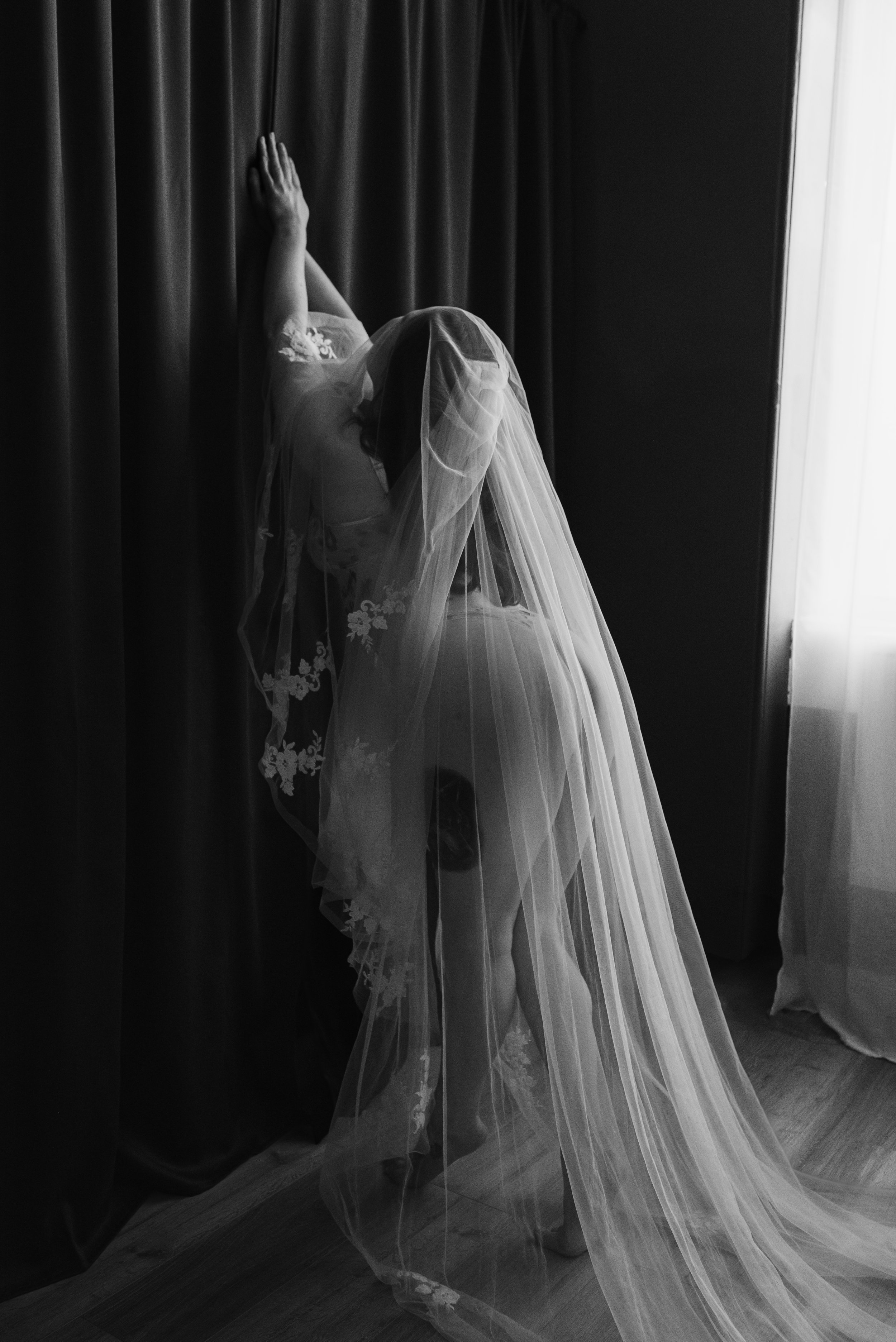 Bridal boudoir photography Glasgow — woman holding wedding veil beside window, black and white portrait