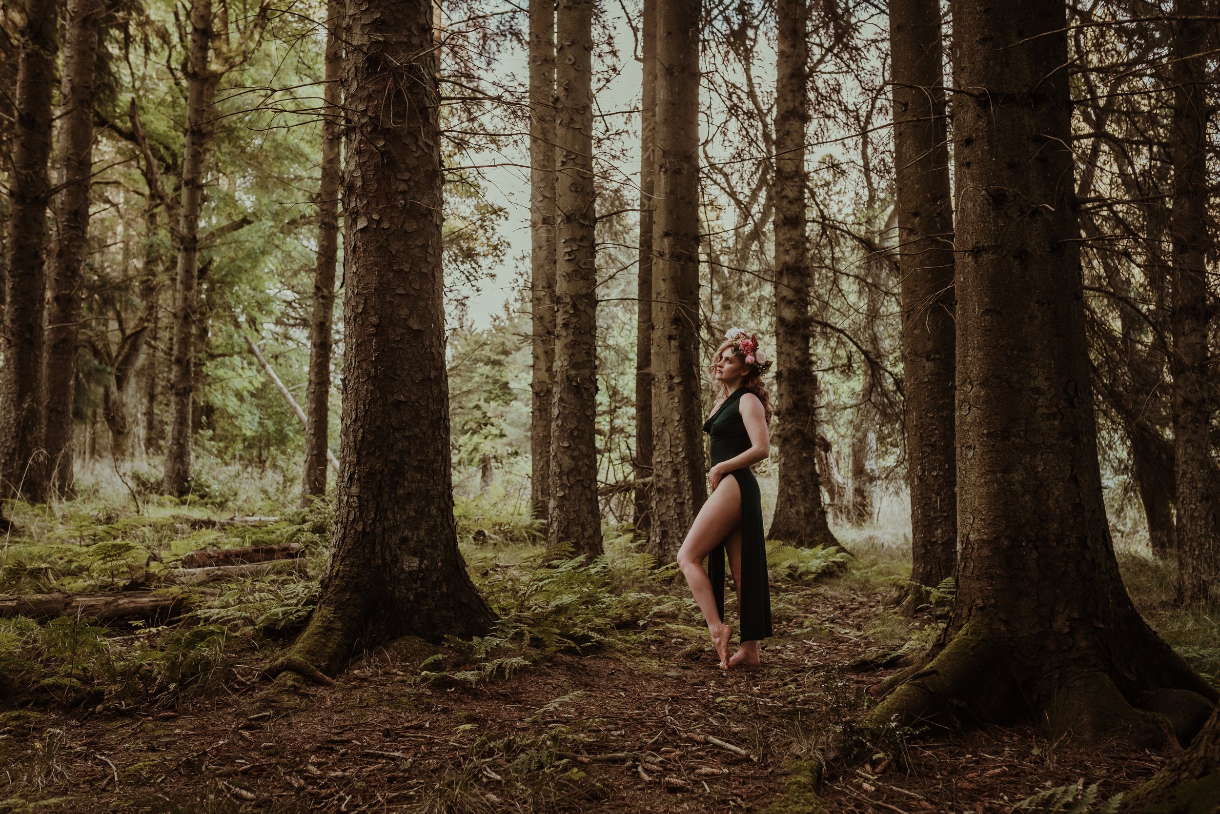 Woman in a flowing green dress with a dramatic high split during an adventure boudoir photography session in a forest near Stirling, Scotland with Marieke Captures — elegant, wild and utterly free
