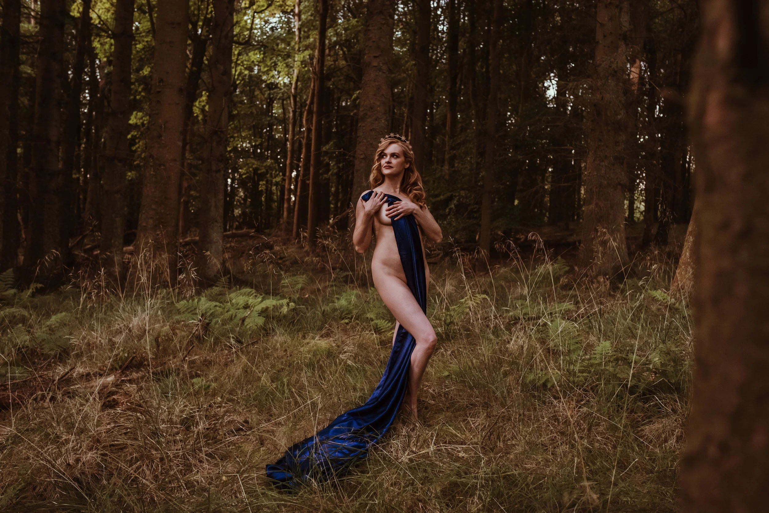Woman standing proudly in a forest near Stirling draped in a blue sheet during an adventure boudoir photography session with Marieke Captures, Scotland — raw, powerful and beautifully connected to nature