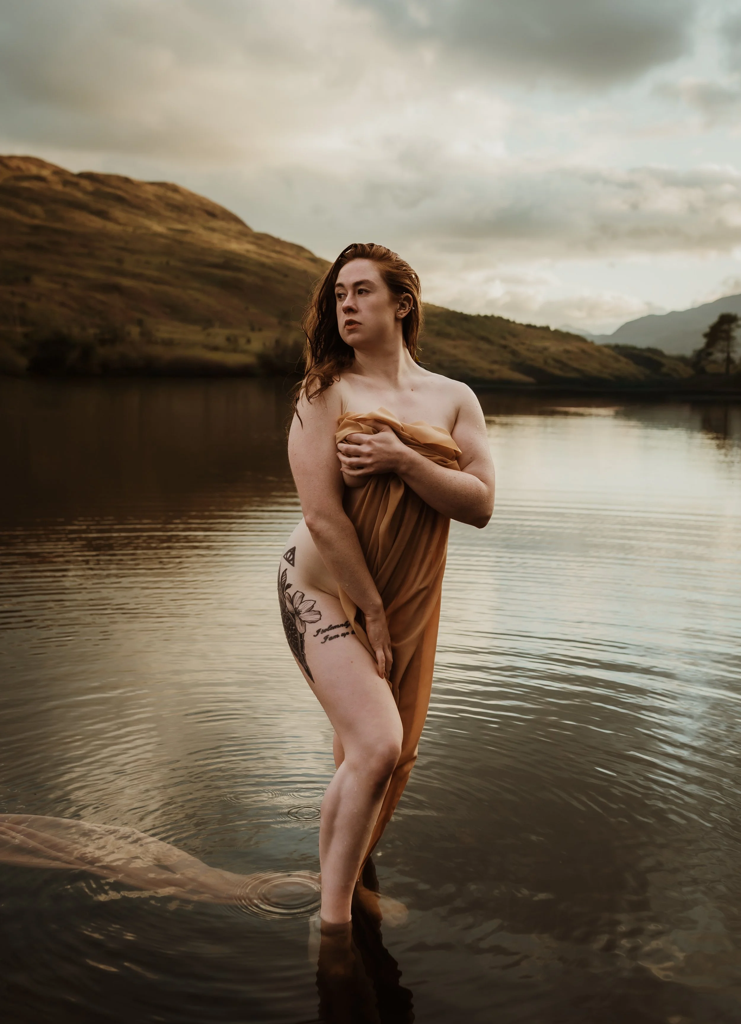 Outdoor boudoir photography Scotland — woman standing in Scottish loch with highland hills in background