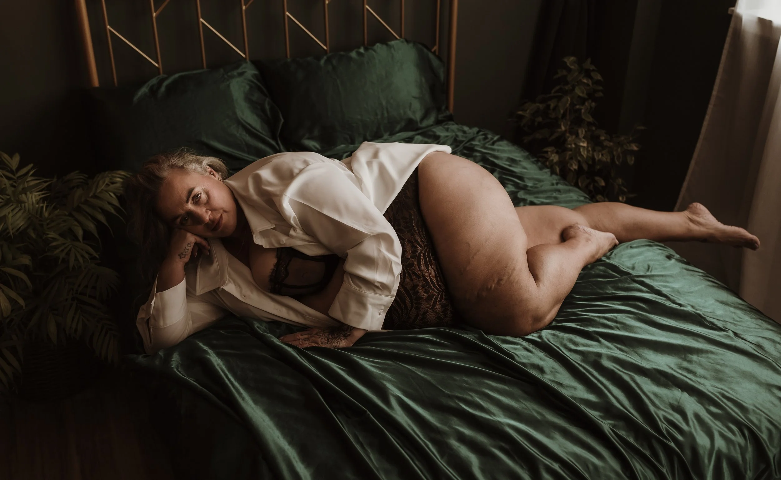 Woman in an open white satin shirt and lace lingerie reclining on green velvet bedding during a boudoir photography session at Marieke Captures studio Glasgow Scotland — soft styling paired with a relaxed, confident pose