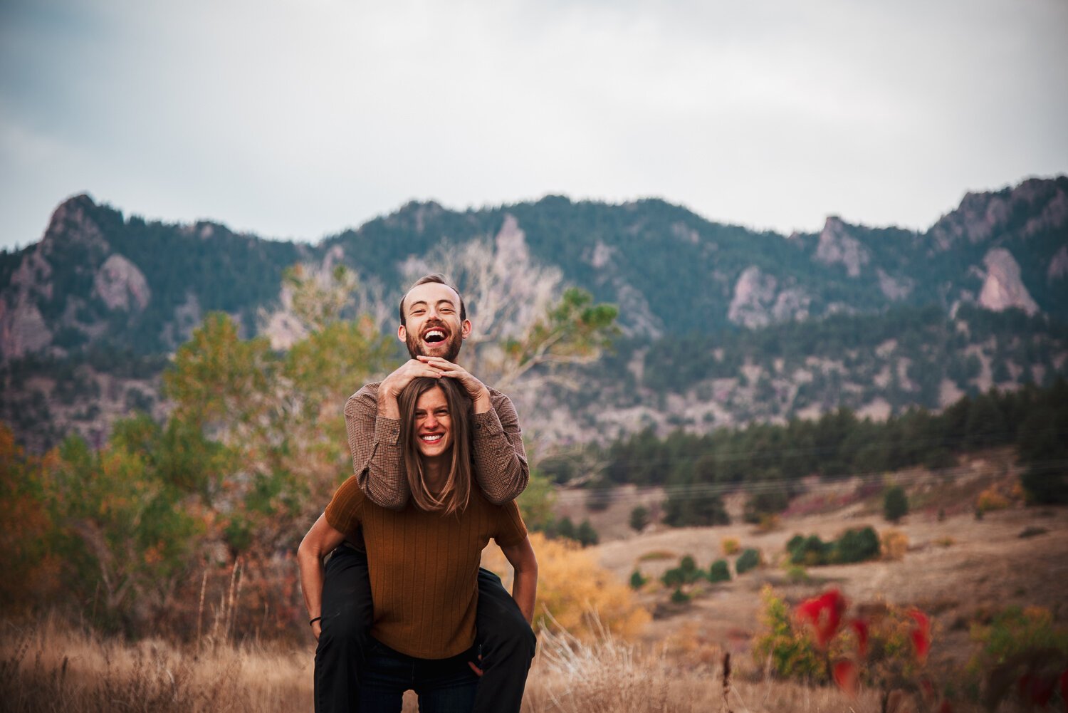 Couple giving each other piggy back ride for engagement photos at South Mesa Trailhead