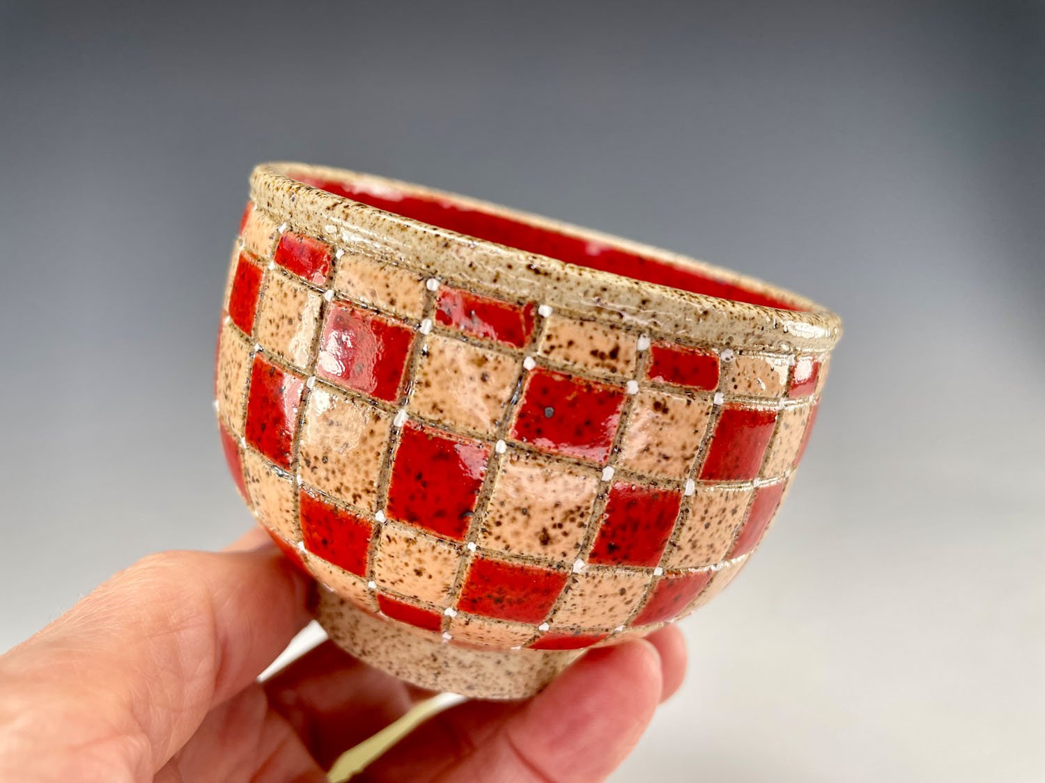 Hand holding Peach red checkerboard stoneware tea bowl