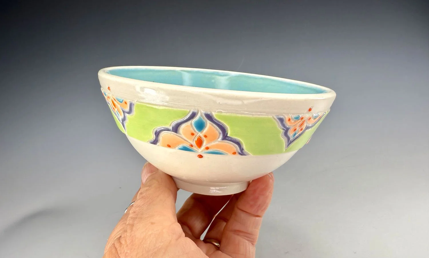 Hand holding bowl 2 of Porcelain snack bowl set w blue liner and hand carved outer designs