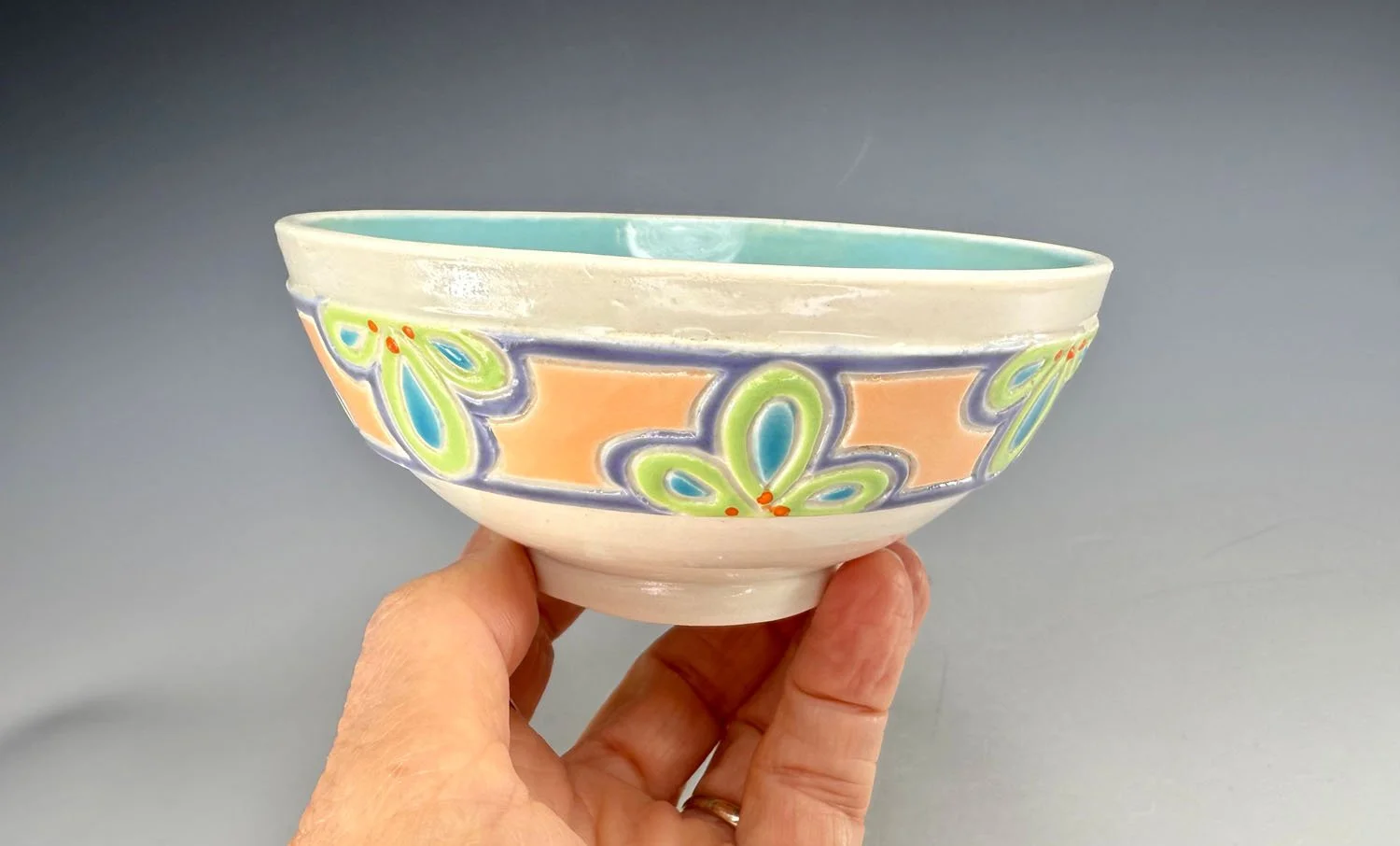 Hand holding bowl 1 of Porcelain snack bowl set w blue liner and hand carved outer designs