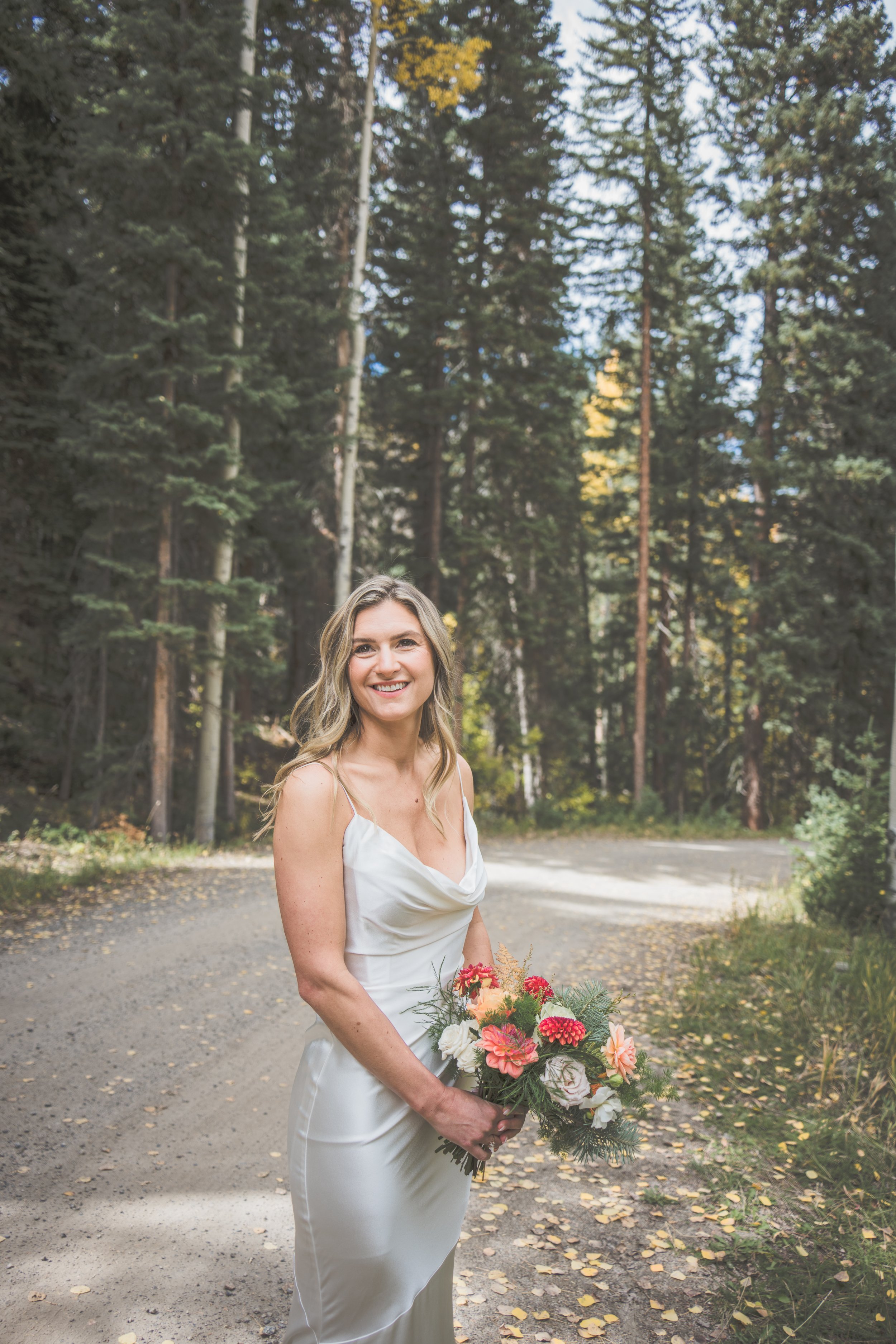 Hand holding a colorful bouquet of various flowers, including dahlias, daisies, black-eyed Susans, and other wildflowers, against a wooden fence background.