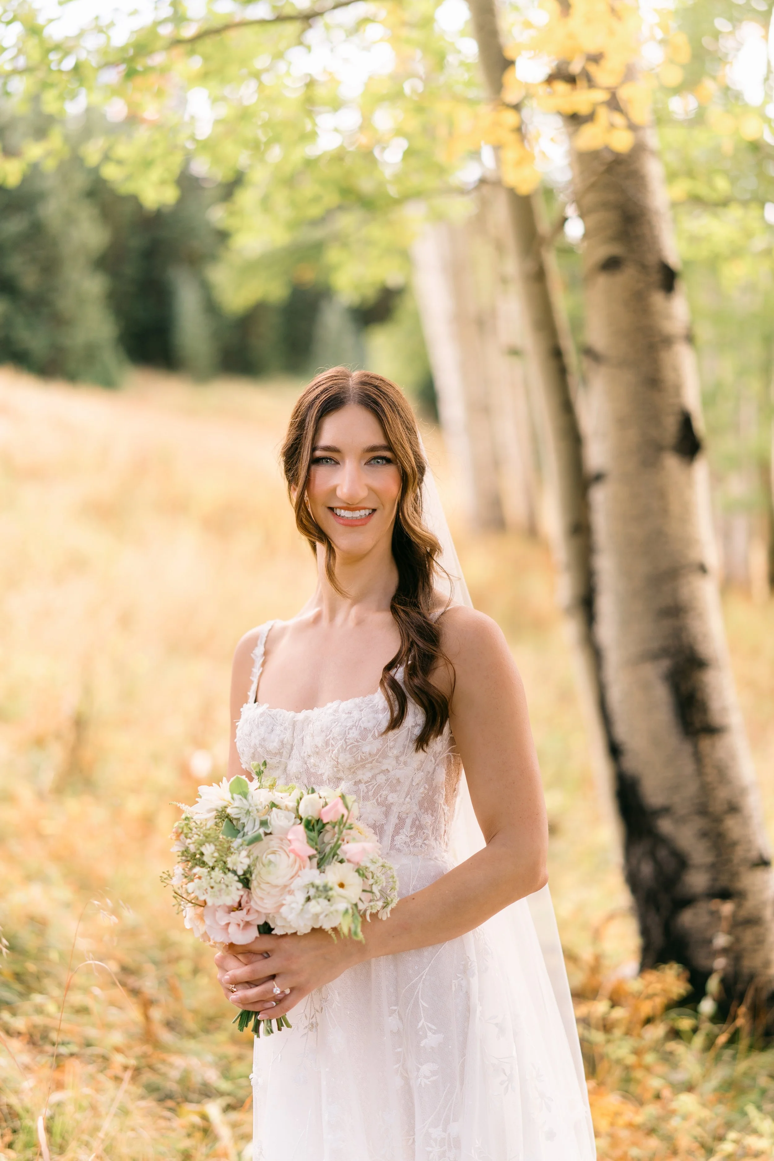 A hand holding a colorful bouquet of mixed flowers in front of a wooden fence with a faint rainbow arching overhead.