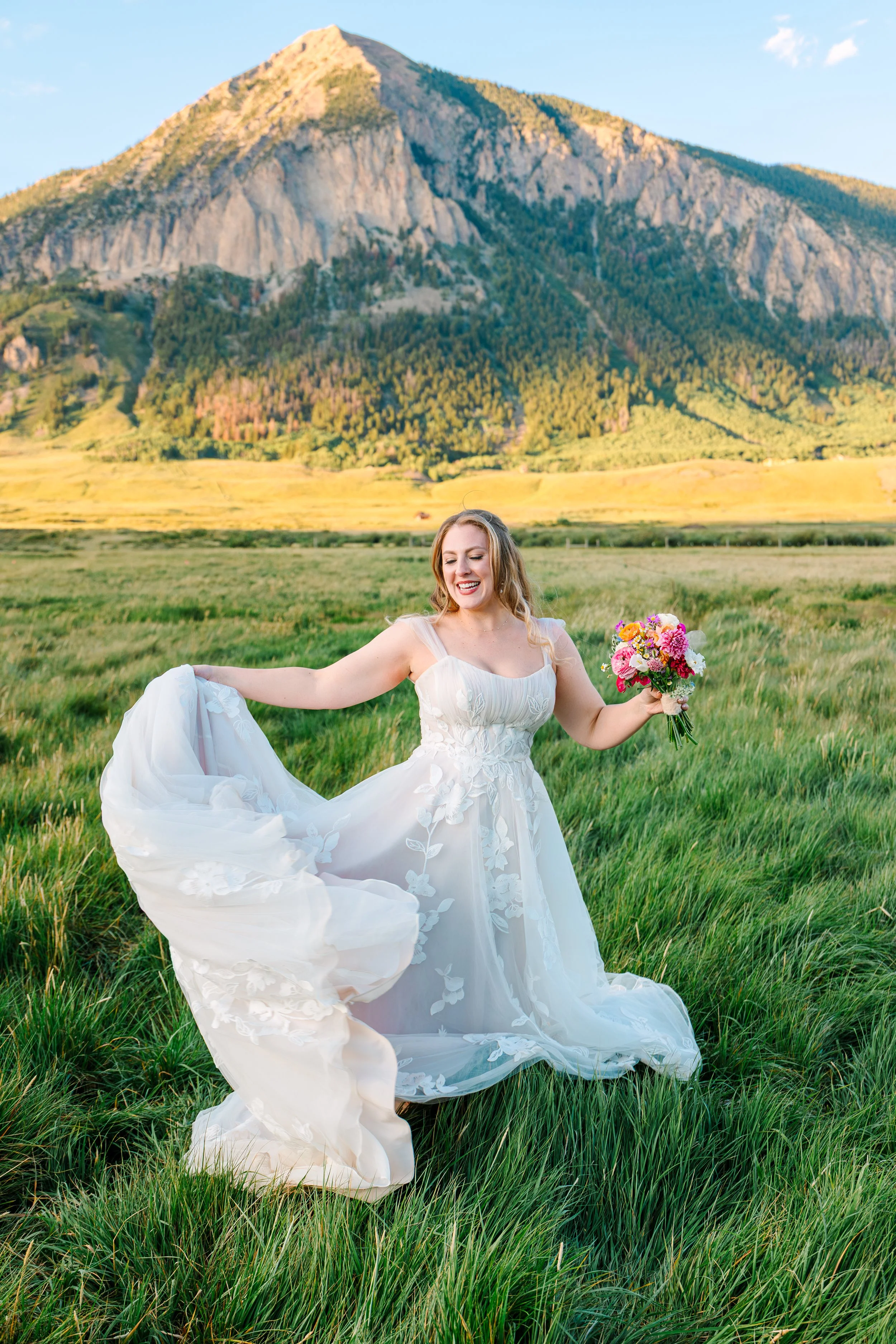 Colorful bouquet of mixed flowers held by a person's hand in front of a rustic wooden fence.
