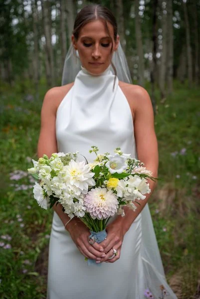 A hand holding a colorful bouquet of flowers with a brown wooden wall in the background.