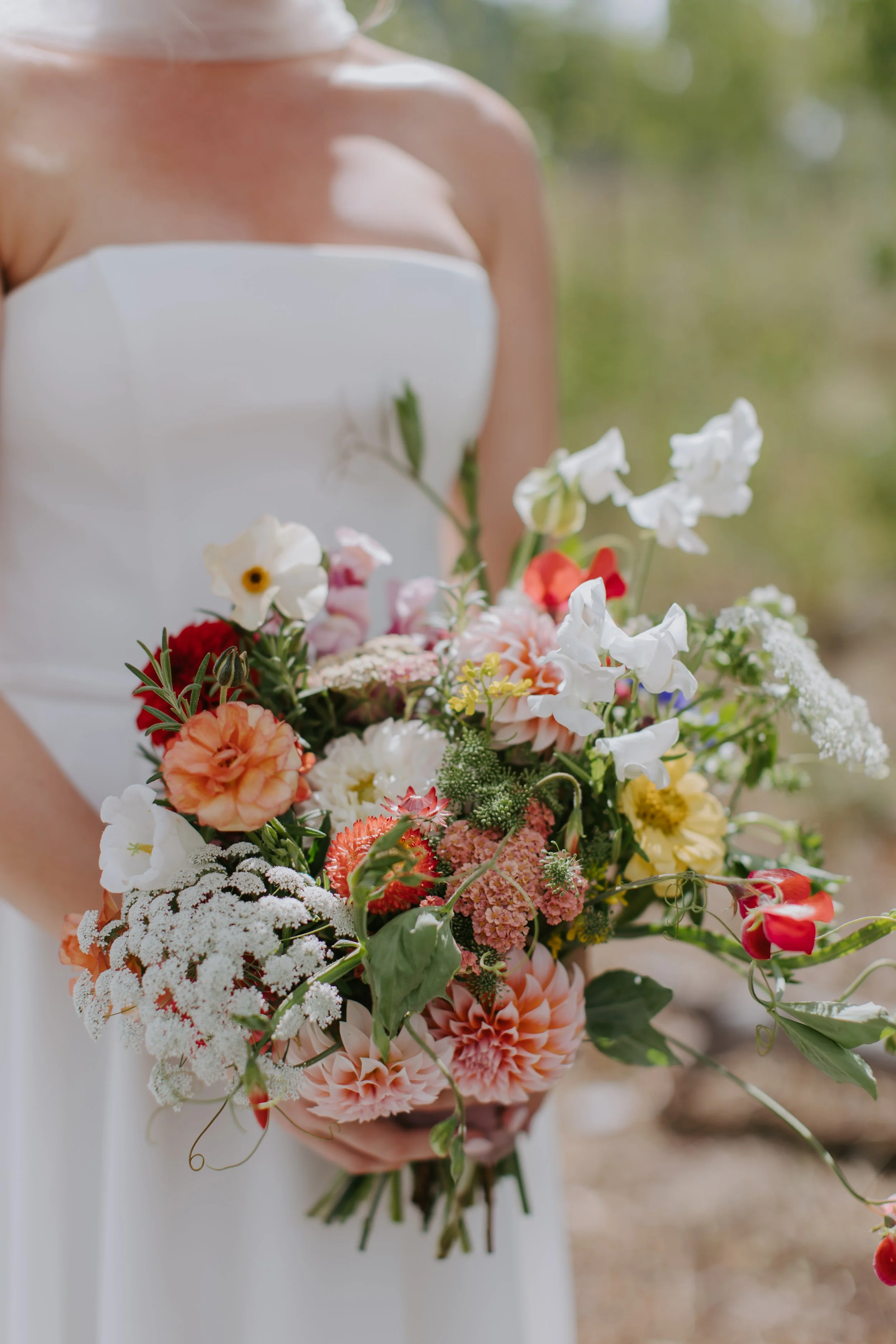 A person's hand holding a bouquet of various colorful flowers with a white ribbon against a wooden background.