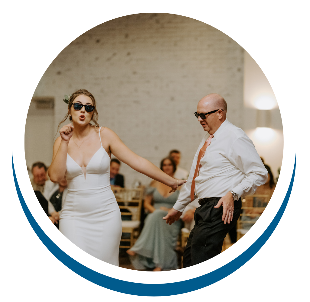Woman in white dress and sunglasses dancing with a bald man in white shirt and tie at a wedding reception.
