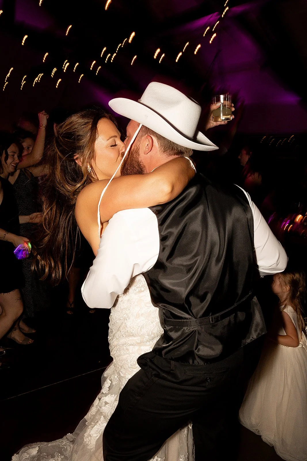 A bride and groom sharing a kiss while dancing at a wedding reception, with guests in the background.