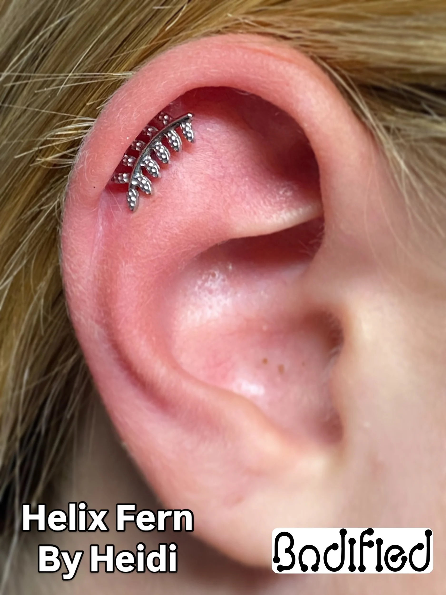 Close-up of a person's ear with a helix fern ear cuff jewelry piece, pink skin, and light blond hair visible.
