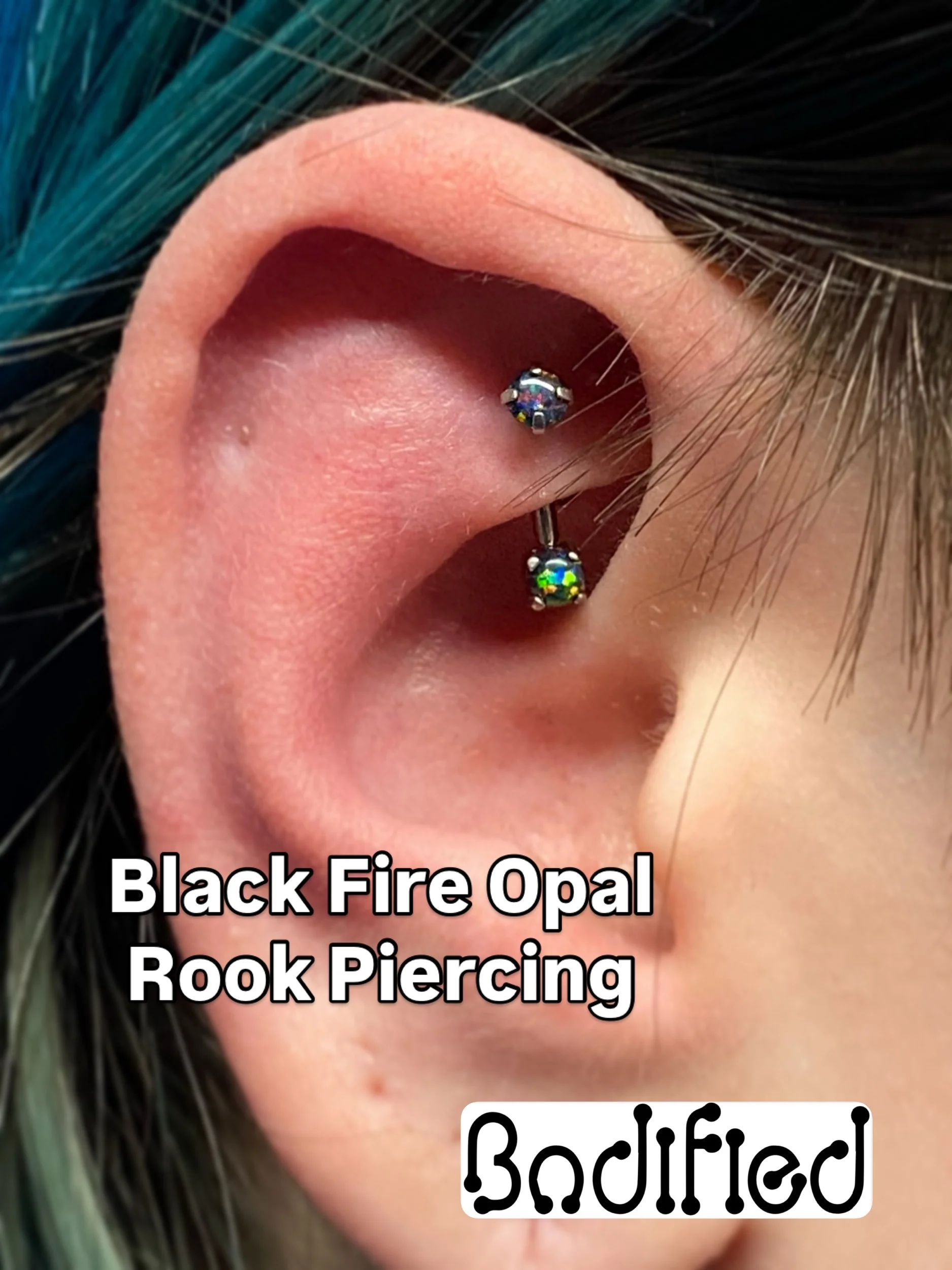 Close-up of a person's ear showing a black fire opal rook piercing with two gemstones, one above the other, in the rook area of the ear.