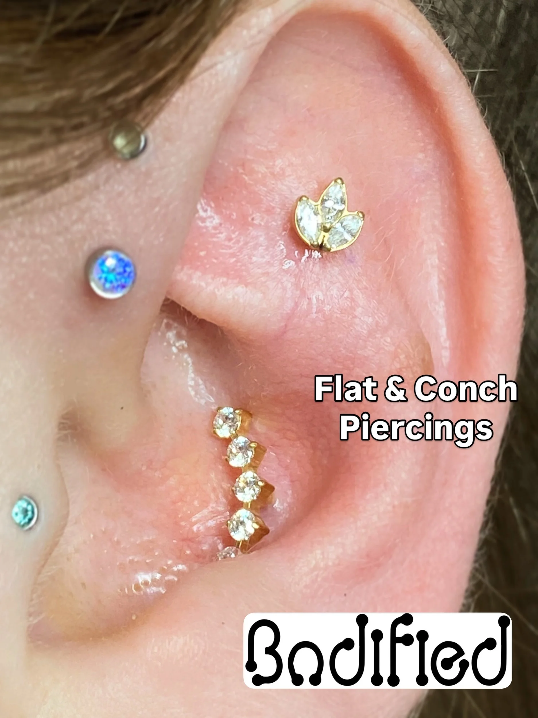 Close-up of multiple piercings on a person's ear with decorative jewelry, including a gold butterfly-shaped stud, a vertical row of gold and diamond studded piercings, and smaller colorful stones. The image includes the text "Flat & Conch Piercings" 