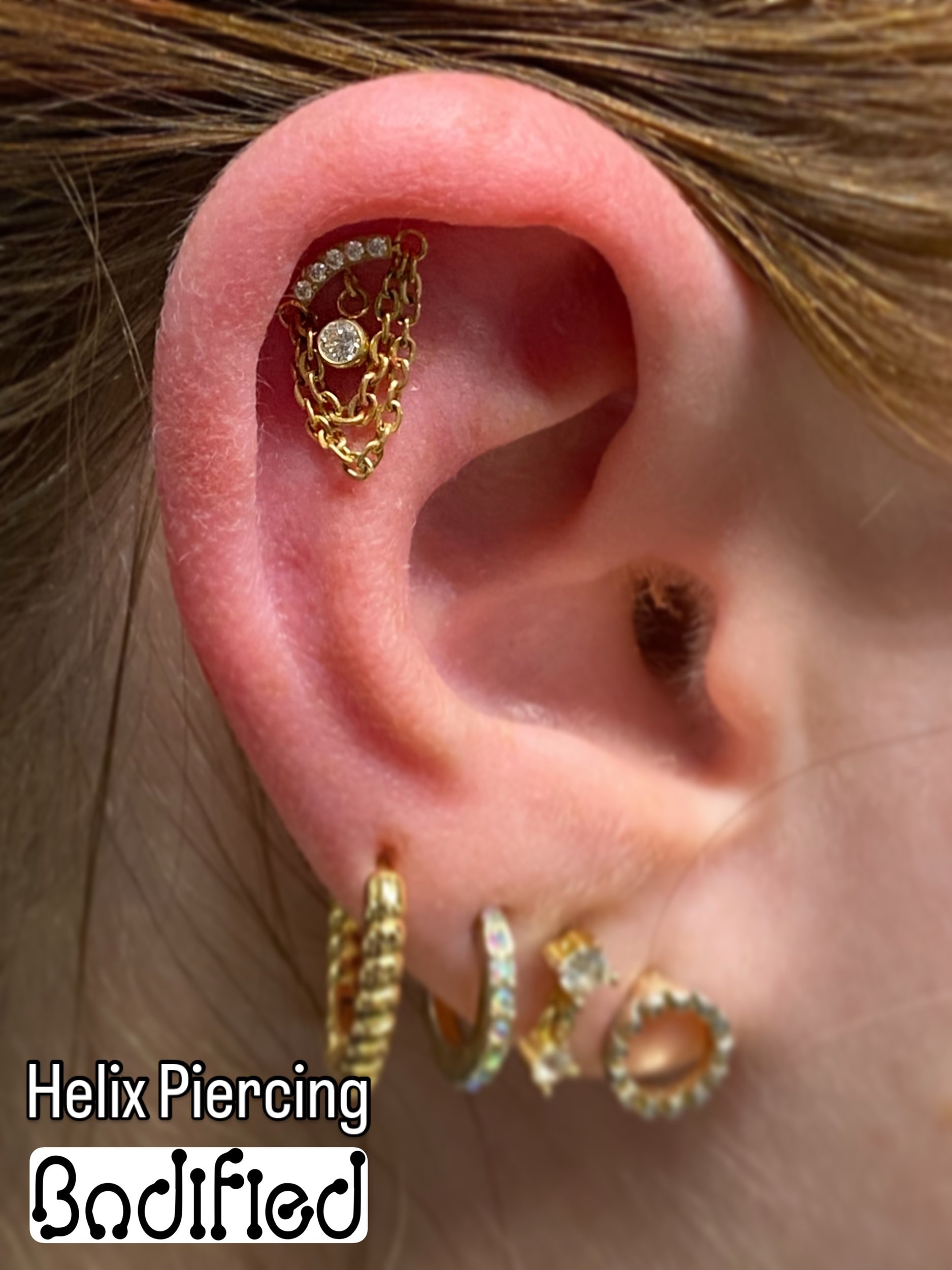 Multiple gold earrings with diamonds and chains in a pierced ear, labeled 'Helix Piercing Bodified'.