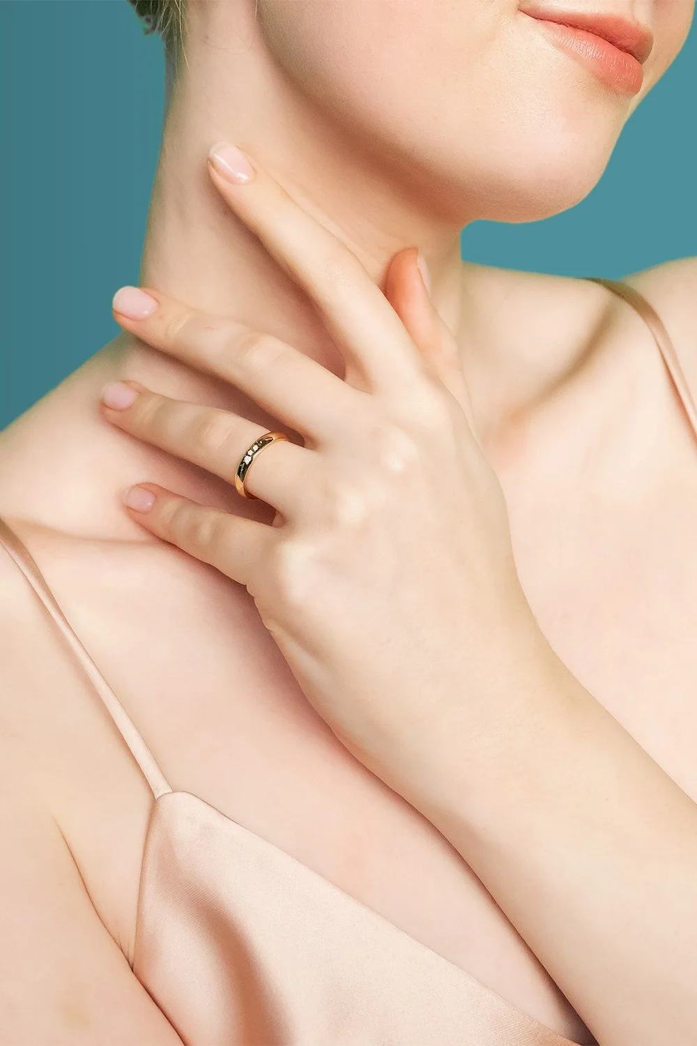 Nahaufnahme einer Frau, die ein Spaghettiträgerkleid trägt und einen Ring hält, mit freundlich platzierten Händen am Hals.