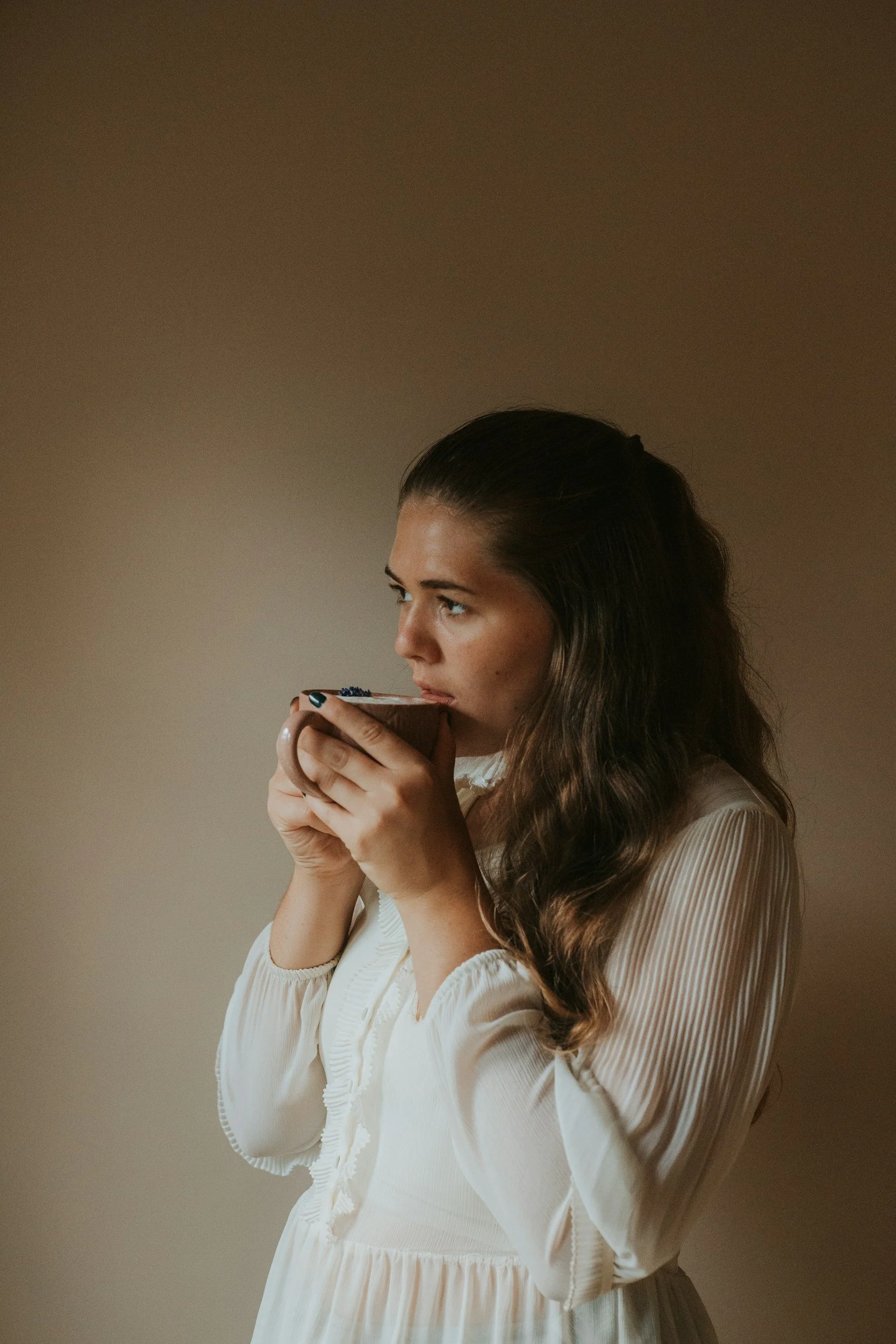 Therapist holding a cup of tea in soft light, representing compassion fatigue and emotional healing.