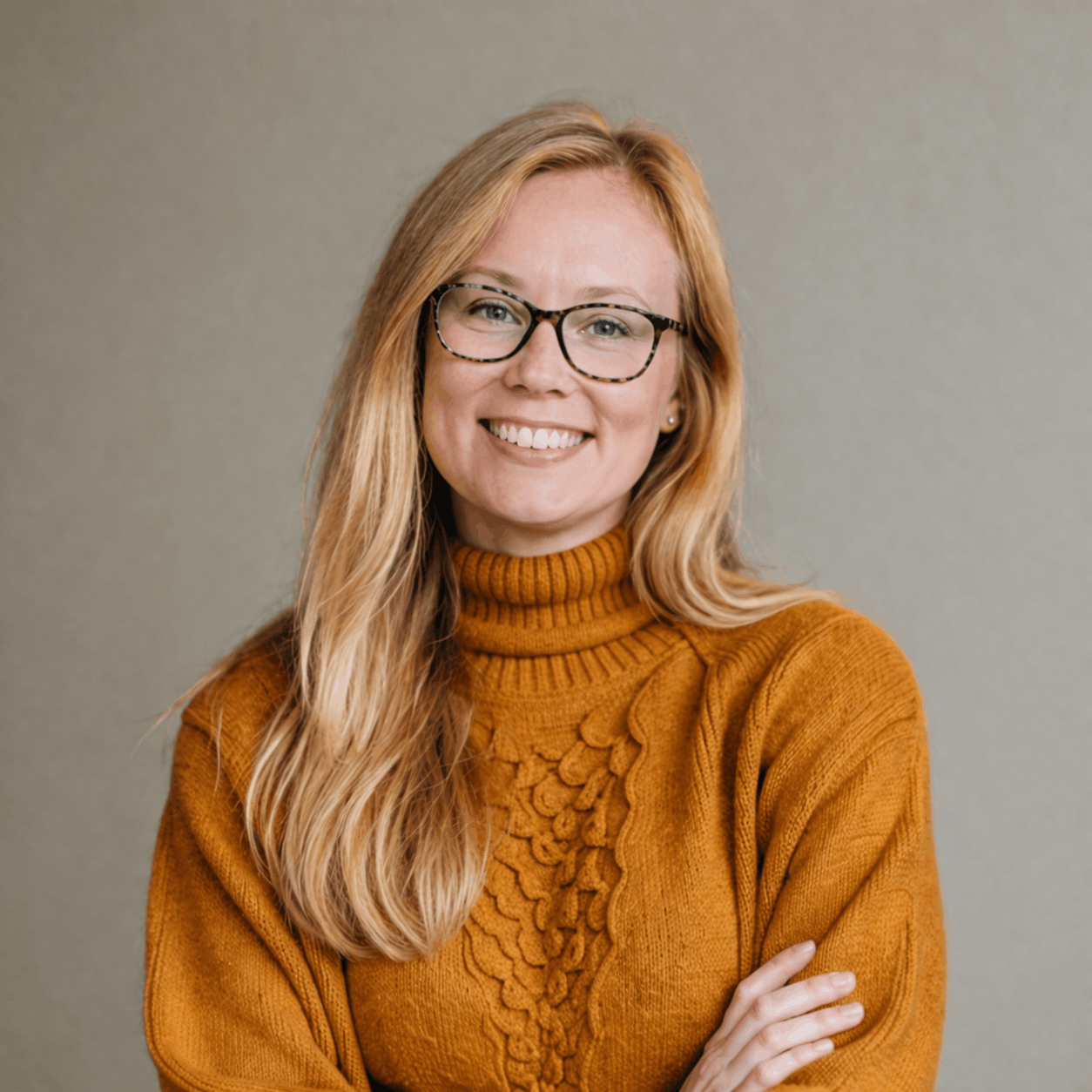 A woman with blonde hair, glasses, and a black shirt smiling against a plain light-colored background.