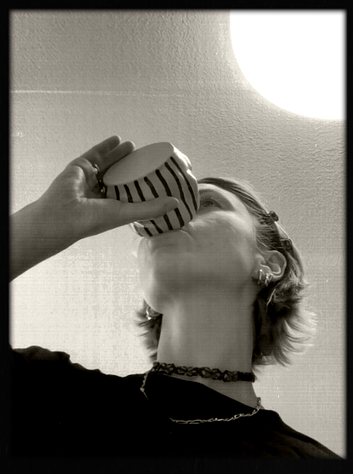 A person drinking from a cup with black and white stripes, viewed from below against a ceiling with a bright light.
