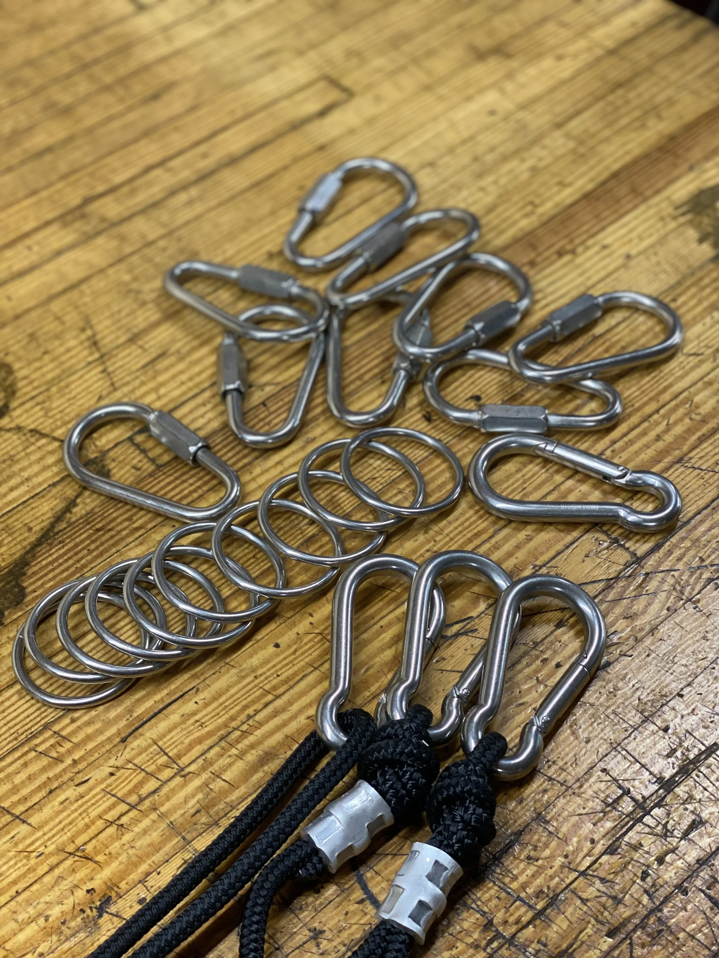 Group of metal carabiners, some attached to black cords with plastic connectors, on a wooden surface.