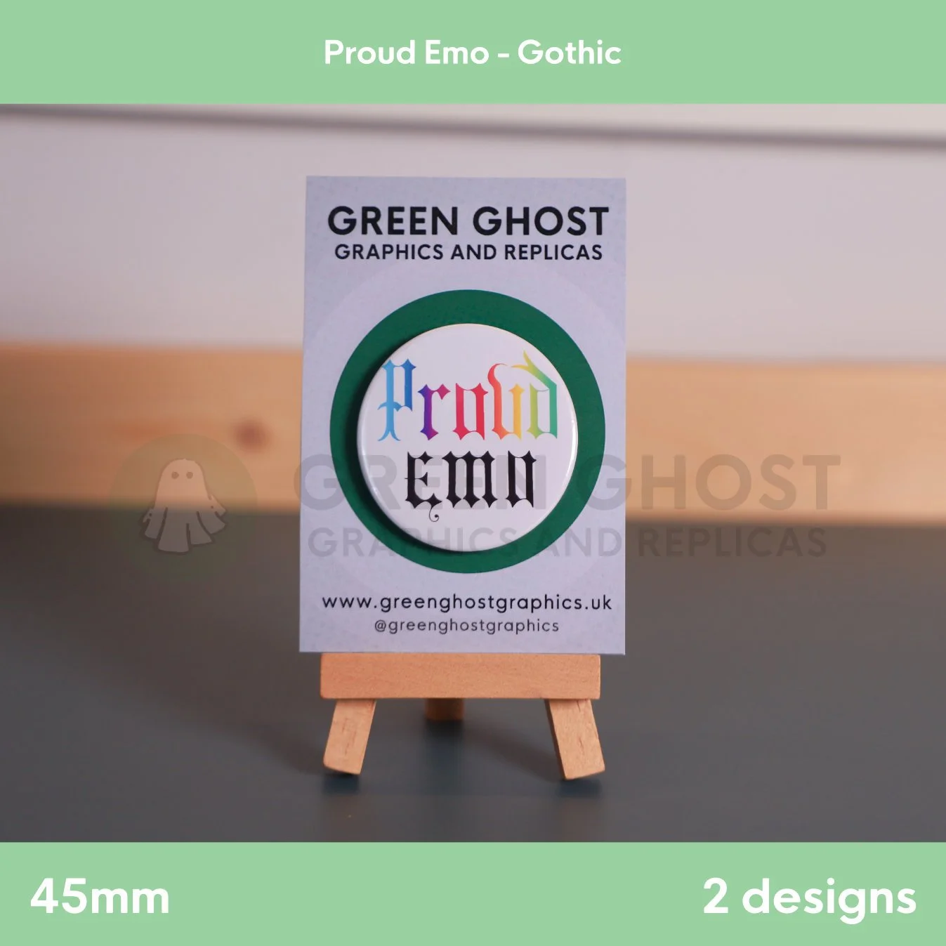 A round white badge with multicoloured “Proud Emo” text displayed on a branded backing card on a wooden easel.