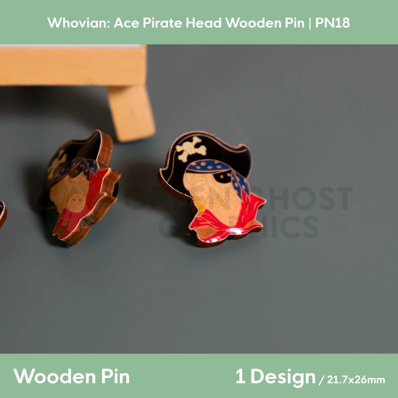 Two colourful pirate‑head wooden pins with black hats, blue headscarves, and red coats positioned in front of a branded display stand.