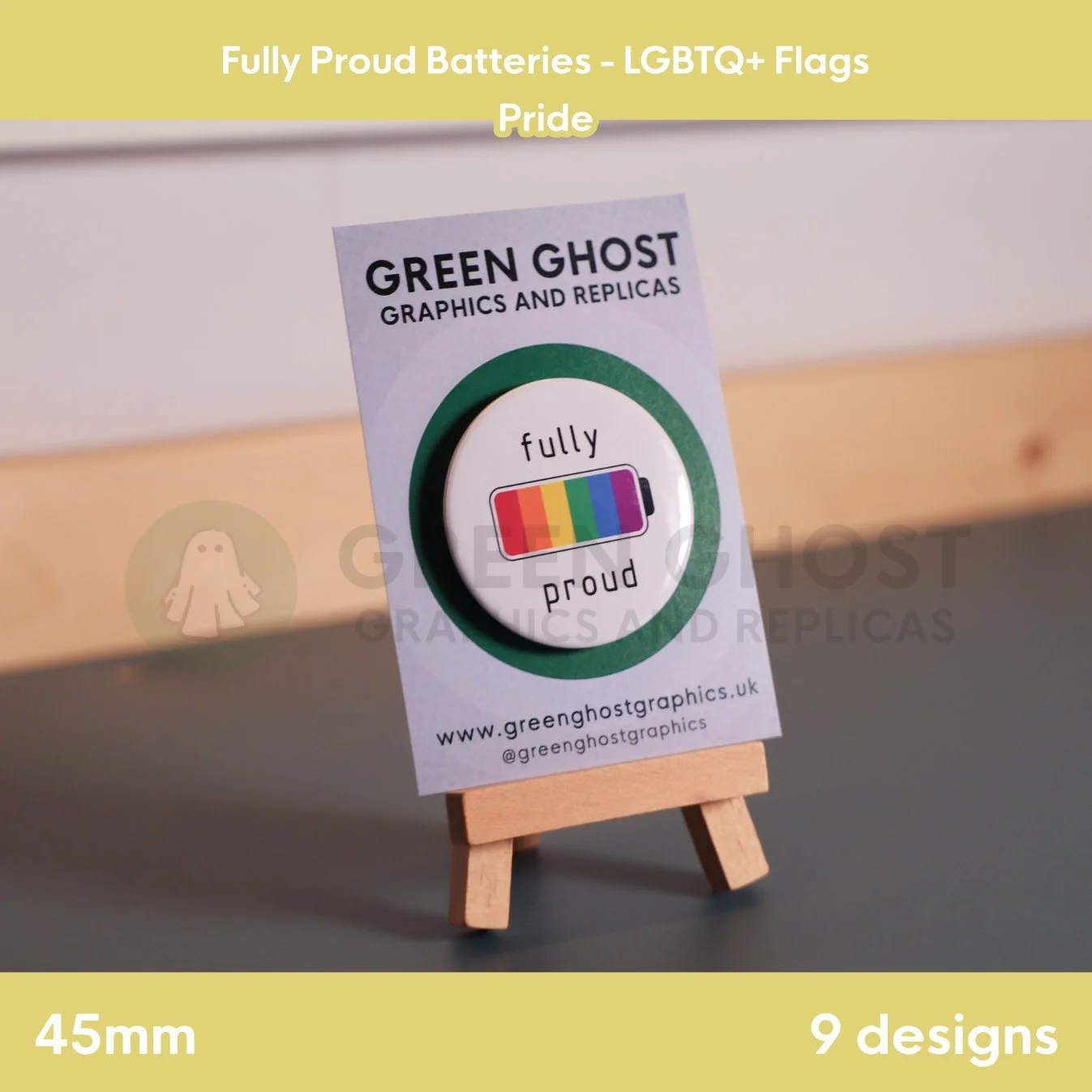 A round badge with a rainbow battery design displayed on a branded backing card on a wooden easel.