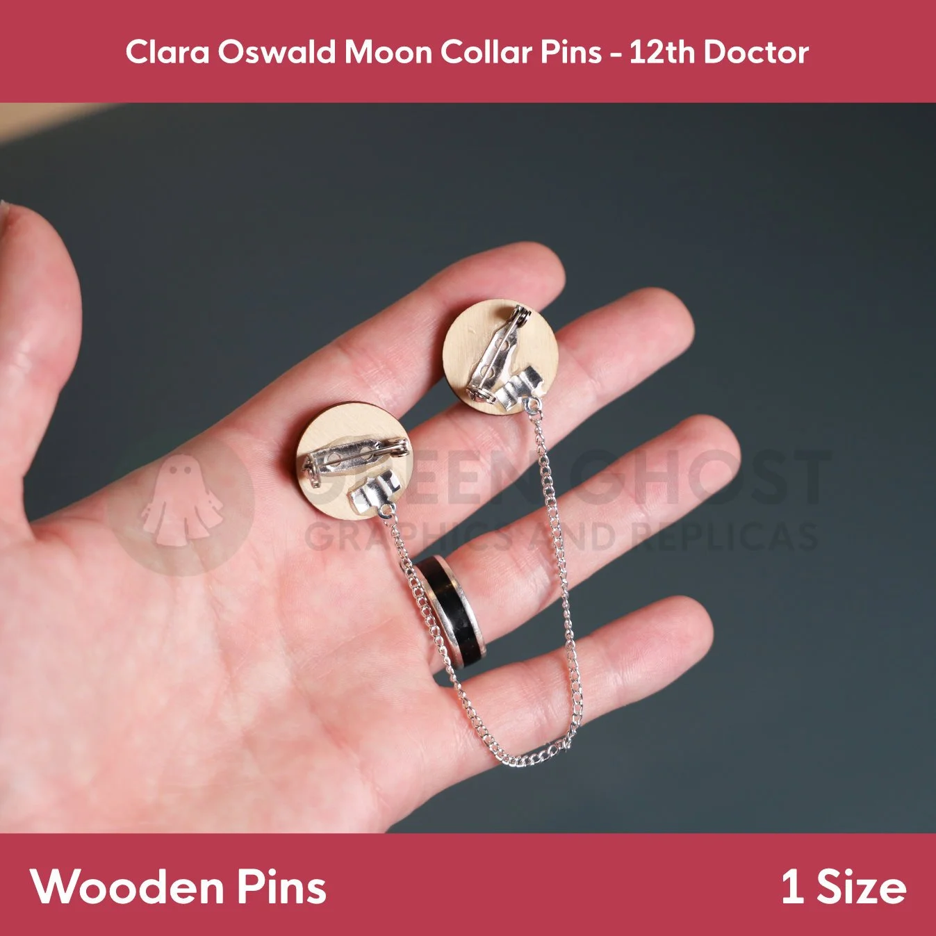 A pair of wooden collar pins with moon artwork and metal backs shown in a hand with the connecting chain visible.