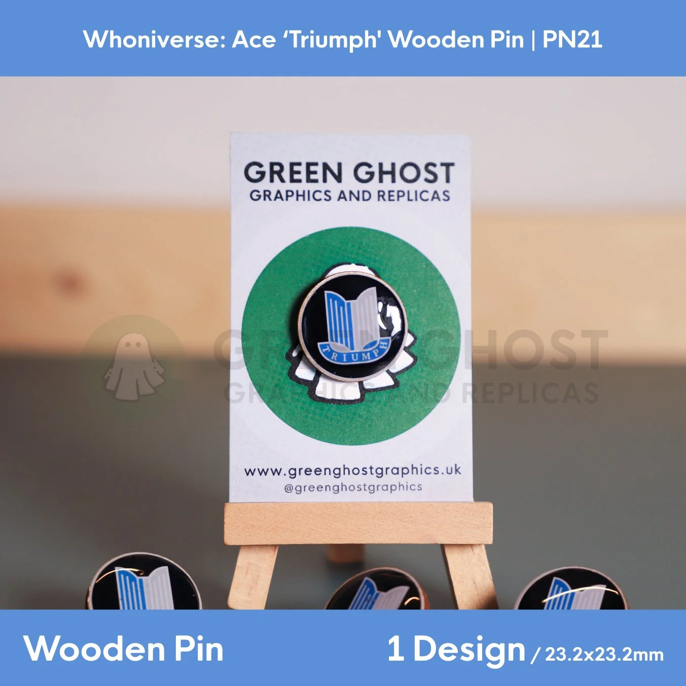 A circular wooden “TRIUMPH” pin mounted on a branded backing card on a wooden easel, with other pins partially visible at the bottom of the frame.