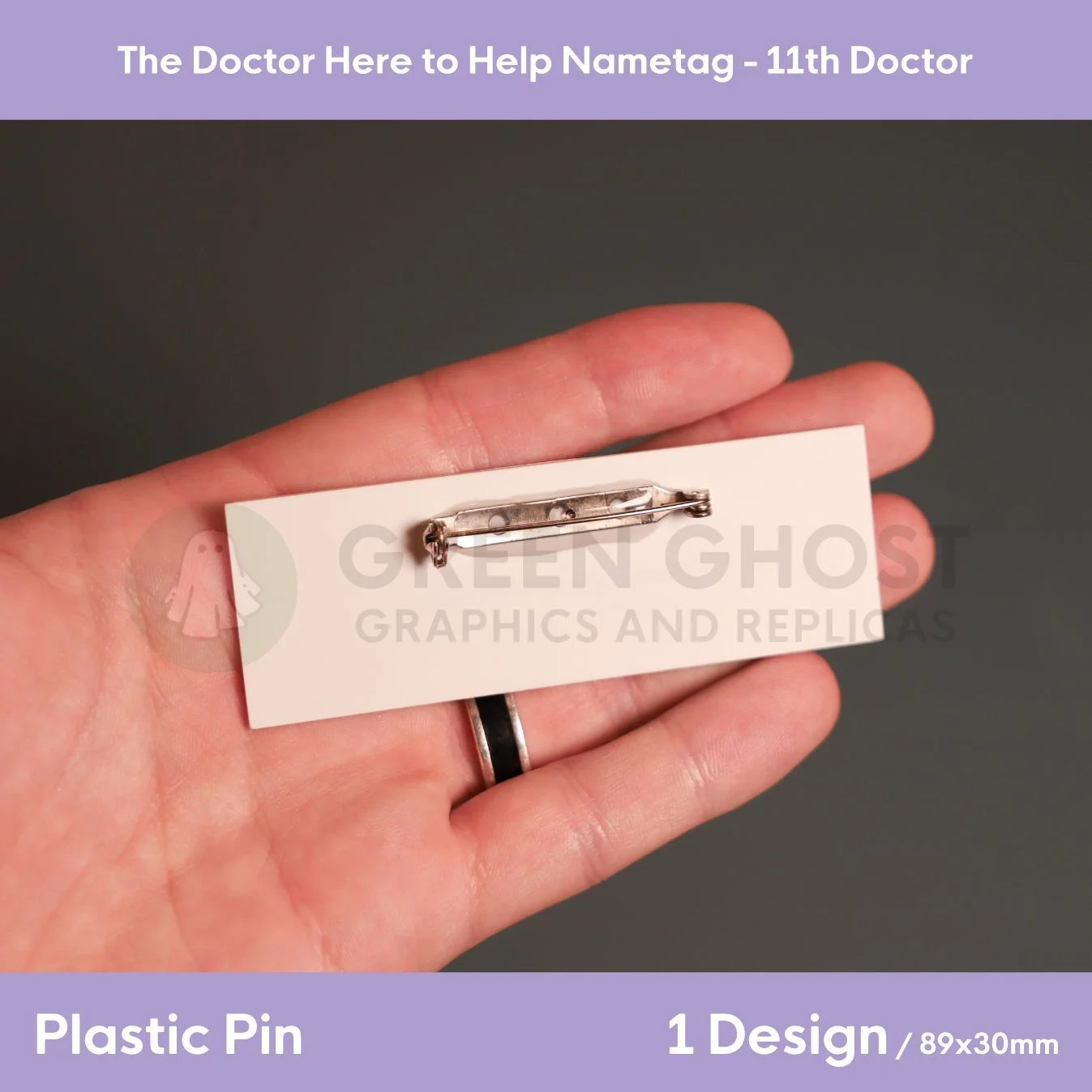 A hand presenting the reverse side of a rectangular plastic nametag with a metal clasp, shown against a plain backdrop.