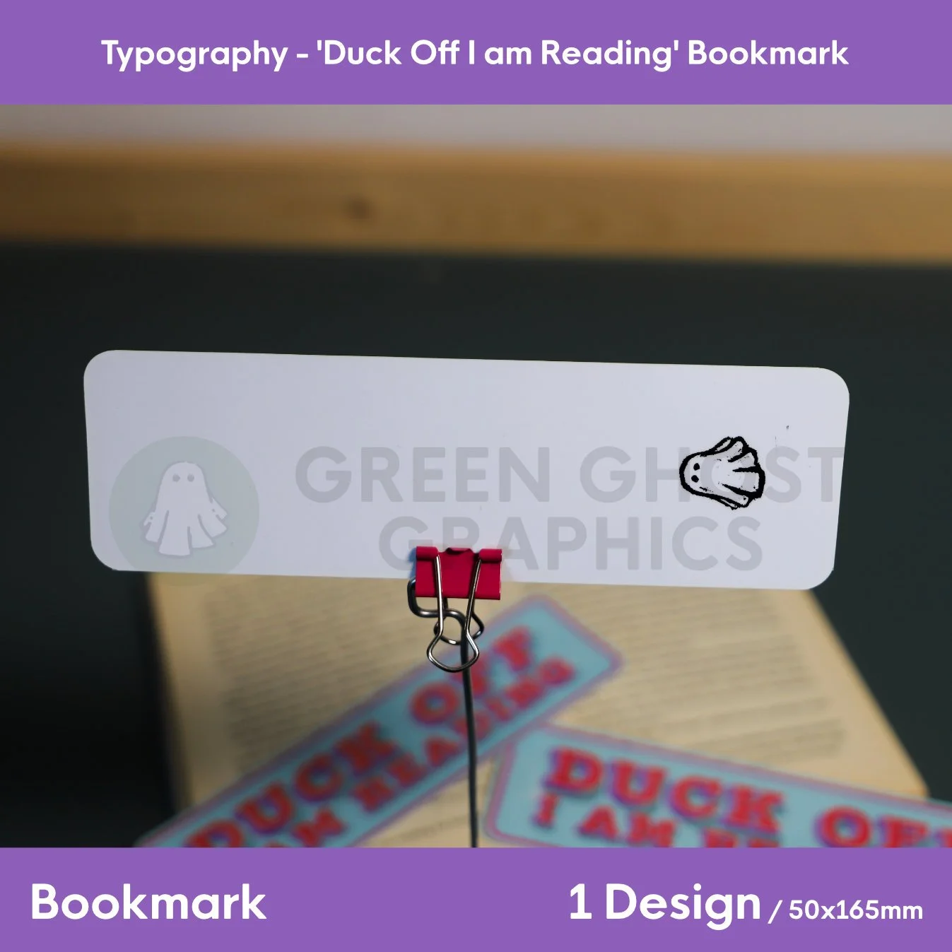 A blue rectangular bookmark printed with “DUCK OFF I AM READING” displayed upright in a clip with open books in the background.