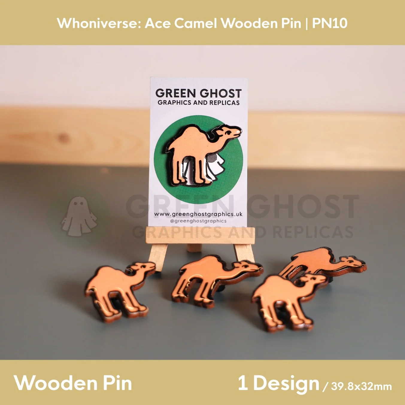 A wooden pin shaped like a stylised camel, mounted on a branded backing card on a wooden easel, with several identical camel pins arranged around it on a grey surface.