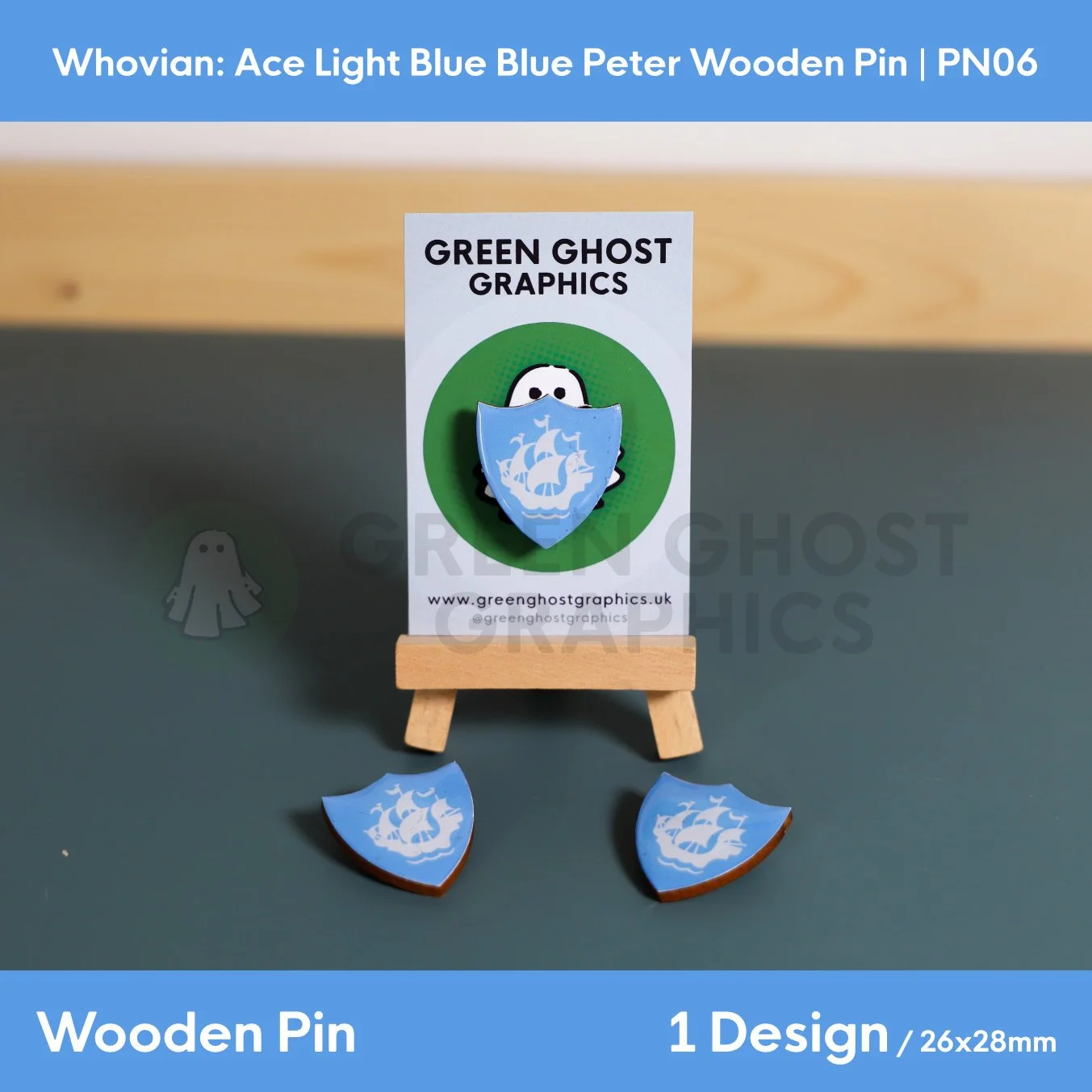 A blue shield‑shaped wooden pin with a white ship emblem presented upright on a clear display rod against a blurred background.