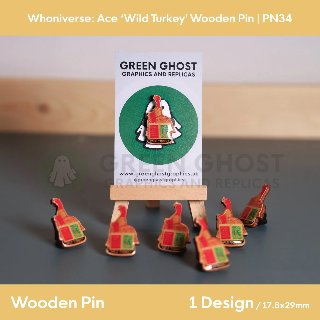 A wooden pin shaped like a turkey and open book attached to a branded backing card on a wooden easel, with several identical pins arranged on the surface in front.