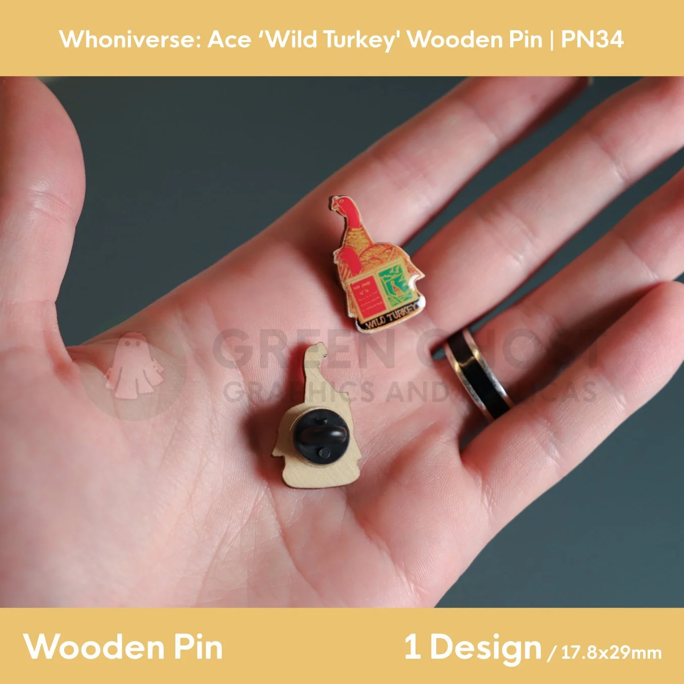 A close‑up of two wooden wild turkey pins held in a hand, showing the detailed Türkiye, book and text design on the front and the rubber pin clasp on the back.